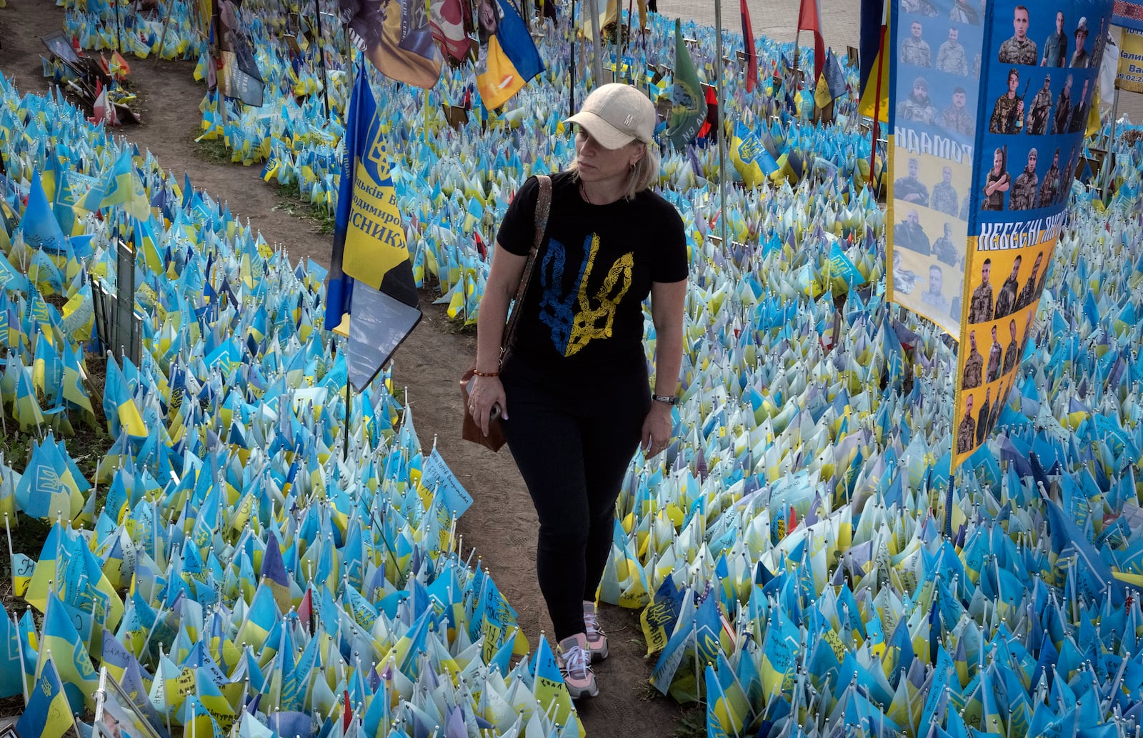 A woman walks through national flags commemorating soldiers who were killed in battles with Russian troops, their names on flags, at the improvised war memorial in Independence Square in Kyiv, Ukraine, Friday, Sept. 27, 2024. (AP Photo/Efrem Lukatsky)