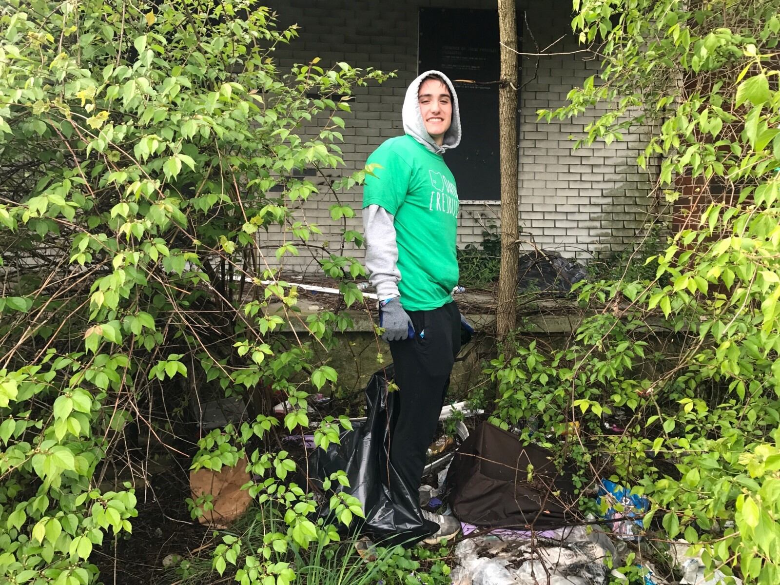 Dayton Flyers wide receiver Luke Brenner works at clearing away some of the overgrowth and trash in front of an abandon house on Weaver Street Saturday as part of the Rebuild Together Dayton effort. (Tom Archdeacon photo)