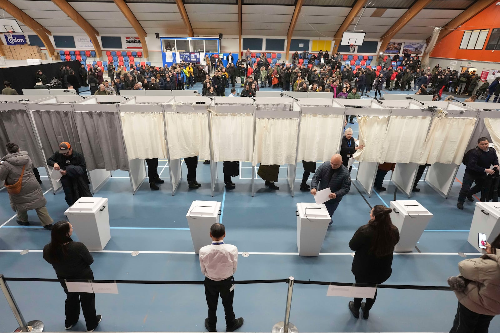 People line up in the back ground to cast their vote in parliamentary elections, in Nuuk, Greenland, Tuesday, March 11, 2025. (AP Photo/Evgeniy Maloletka)