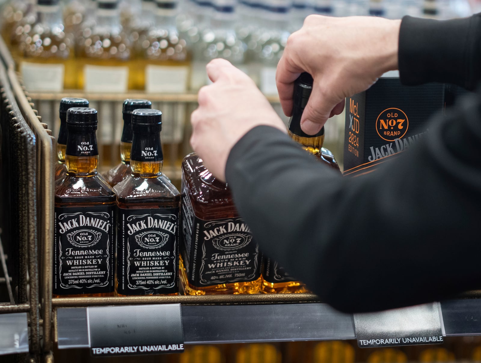 A B.C. Liquor Store employee demonstrates removing bottles of American whiskey for media before a news conference in Vancouver, B.C., Sunday, Feb. 2, 2025. (Ethan Cairns/The Canadian Press via AP)