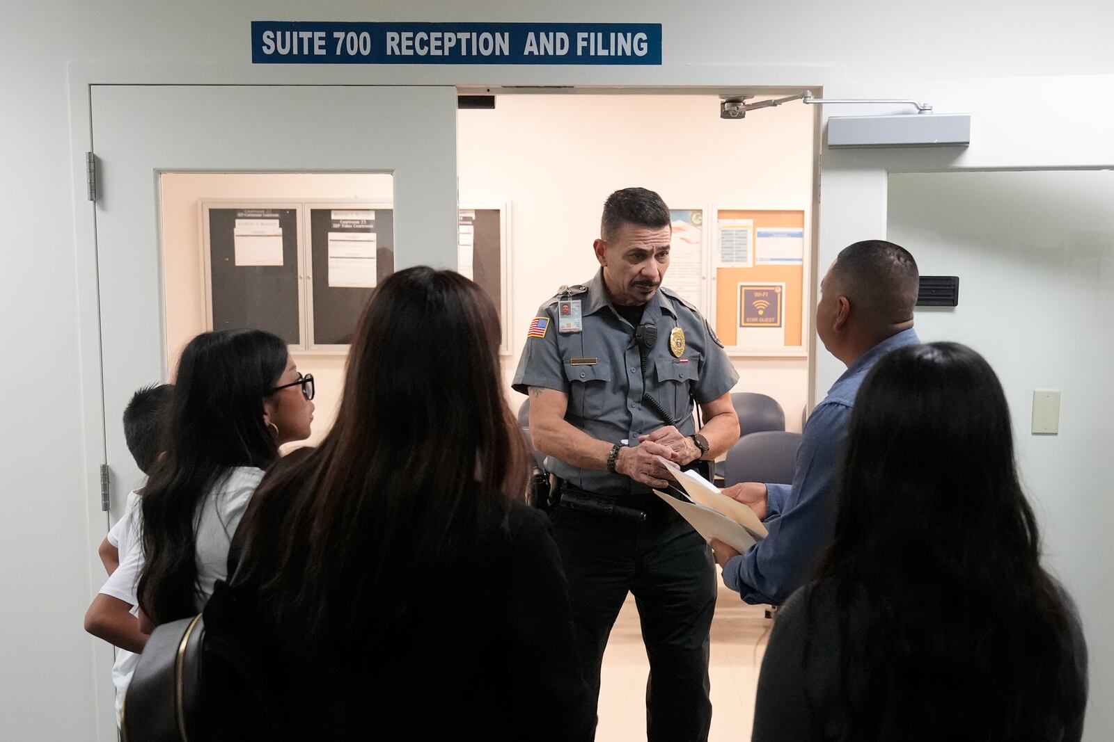 FILE - An officer listens to a question as he directs people to a courtroom, Wednesday, Jan. 10, 2024, in an immigration court in Miami. (AP Photo/Wilfredo Lee, File)