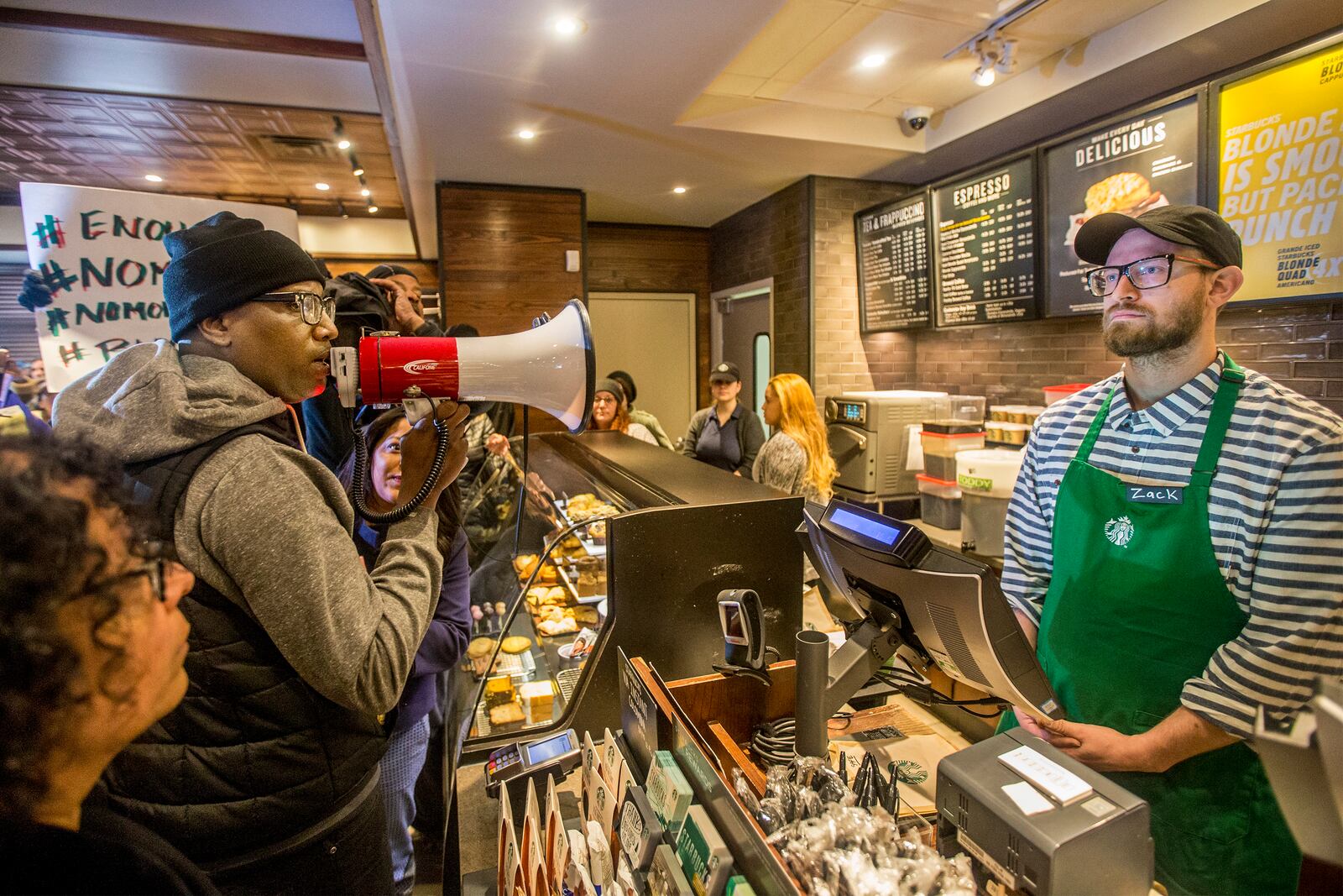 Local Black Lives Matter activist Asa Khalif, left, stands inside the Starbucks at 18th and Spruce, and over a bullhorn, demands the firing of the manager that called police, which resulted in two black men being arrested. On Sunday April 15, 2018, protesters demonstrated outside the Starbucks and planned to return Monday. (Michael Bryant//Philadelphia Inquirer/TNS)