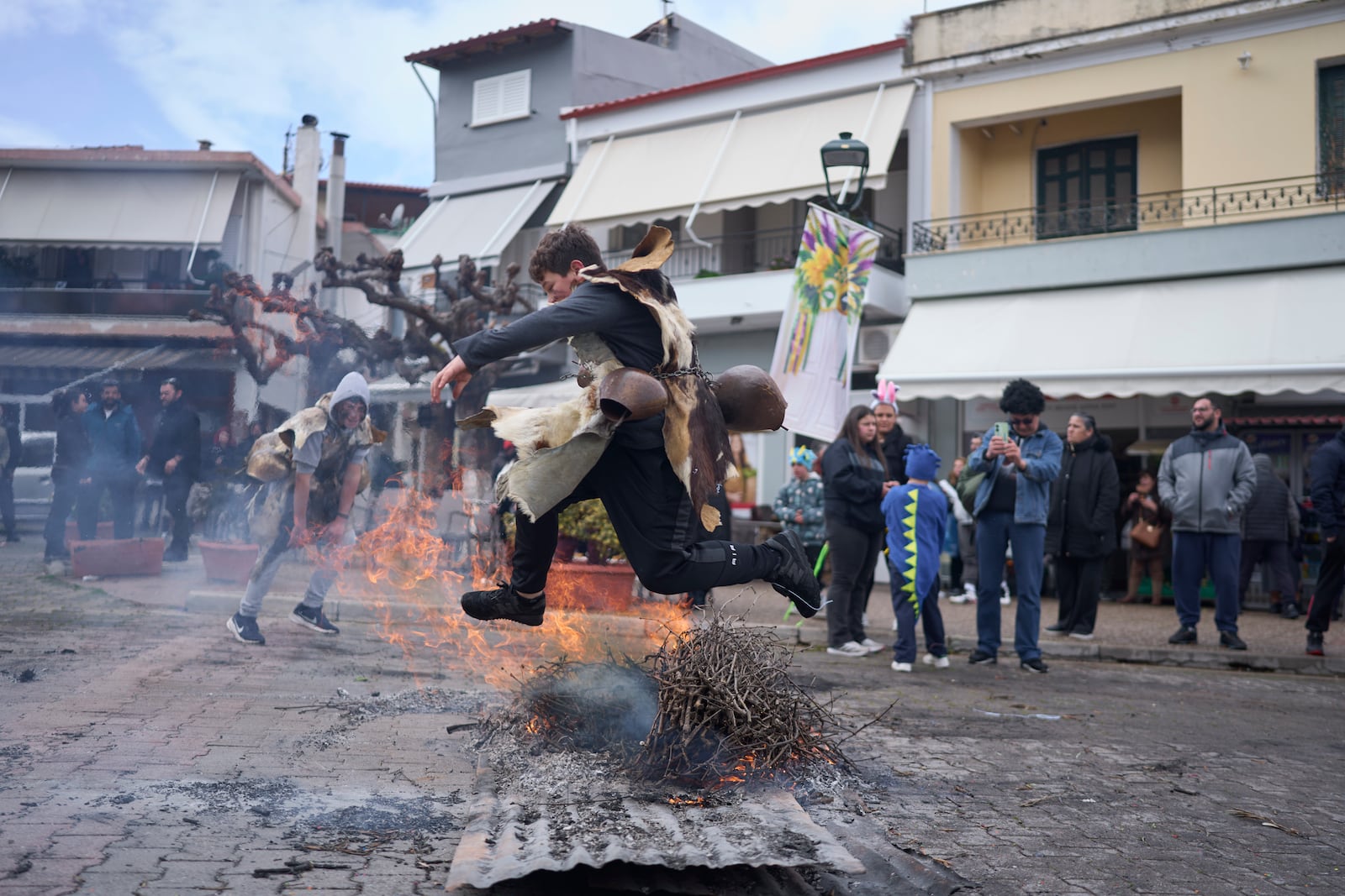 A boy dressed in animal skins and heavy bronze bells, jumps over a burning carnival effigy during carnival celebrations in Distomo, a village in central Greece, on Monday, March 3, 2025. (AP Photo/Petros Giannakouris)