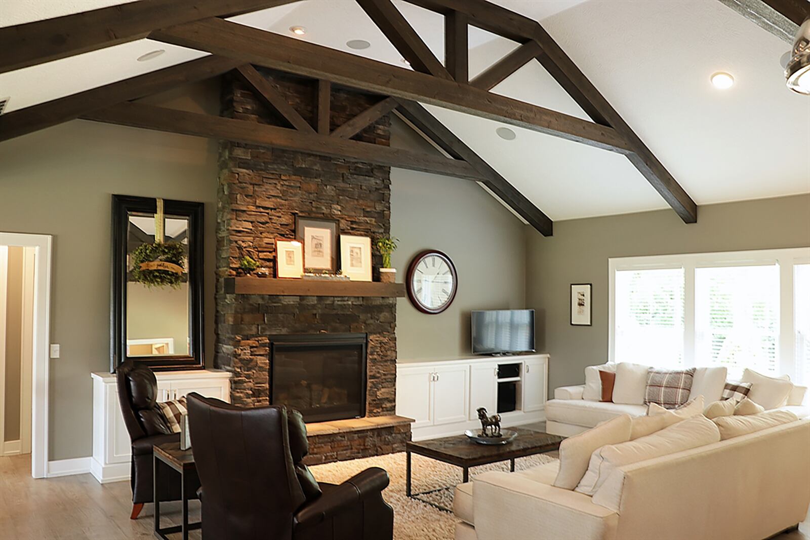 Distressed gray wood flooring fills the foyer and continues into the main social areas that create one space under a gambrel roof with king cross-beam trusses. A stone, gas fireplace with raised hearth and wood-beam mantel is flanked by built-in cabinetry in the great room. CONTRIBUTED PHOTO BY KATHY TYLER