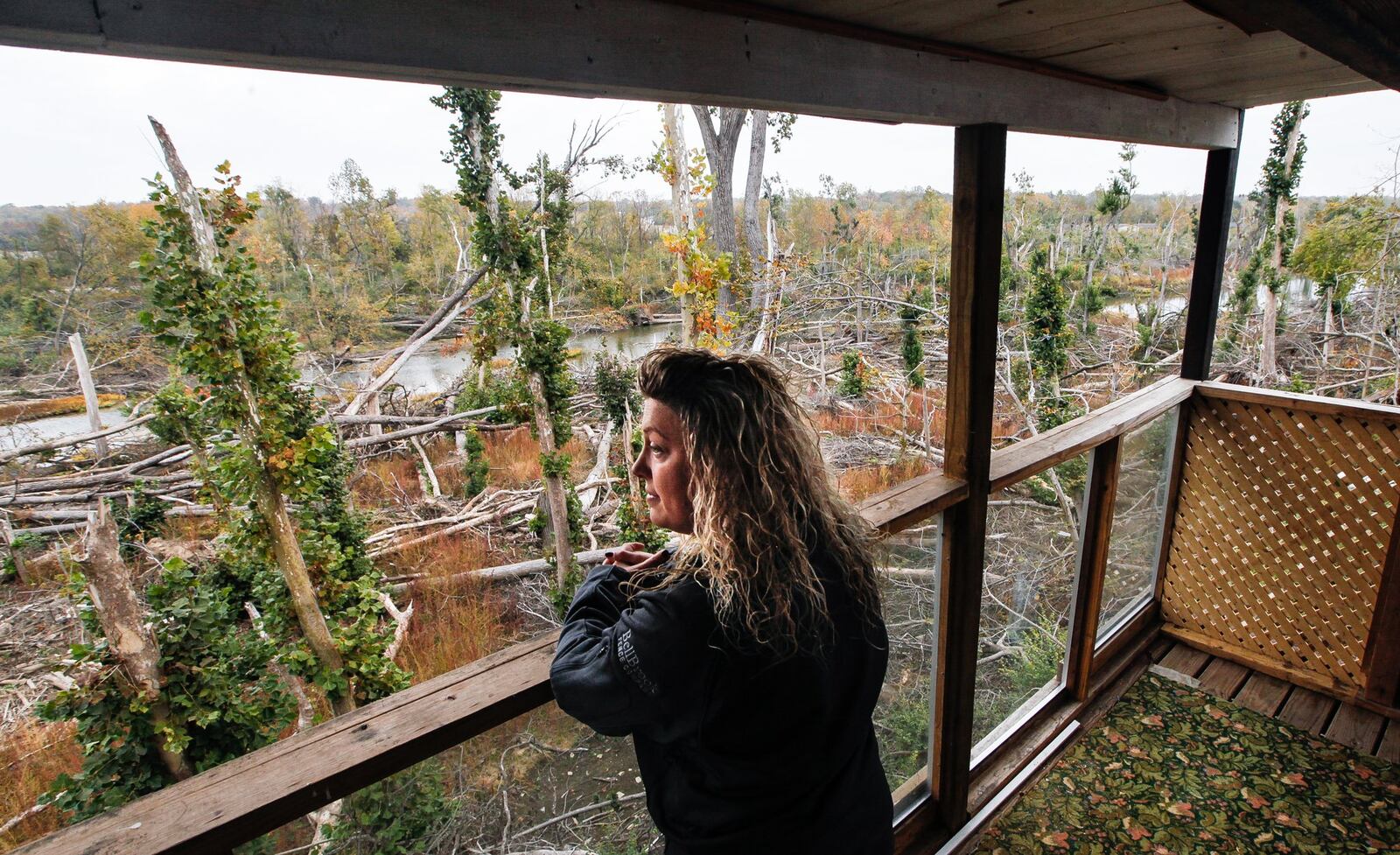 Allison Saldivar looks across the Stillwater River from a balcony on her Lofty Oaks Lane home in Harrison Twp. that was once hidden from view but now exposed after the EF4 took down trees along the riverbank. CHRIS STEWART / STAFF