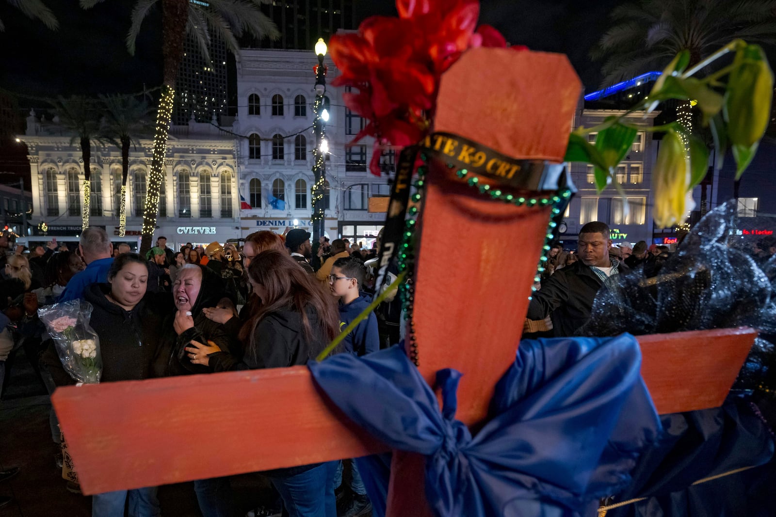 Jessica Perez, holding flowers left, hugs her mother Martha Perez who cries out by a cross memorializing her daughter, Nicole Perez, who was a victim on the New Year's Day attack, on Canal Street near the intersection of Bourbon Street in New Orleans, Saturday, Jan. 4, 2025. (AP Photo/Matthew Hinton)