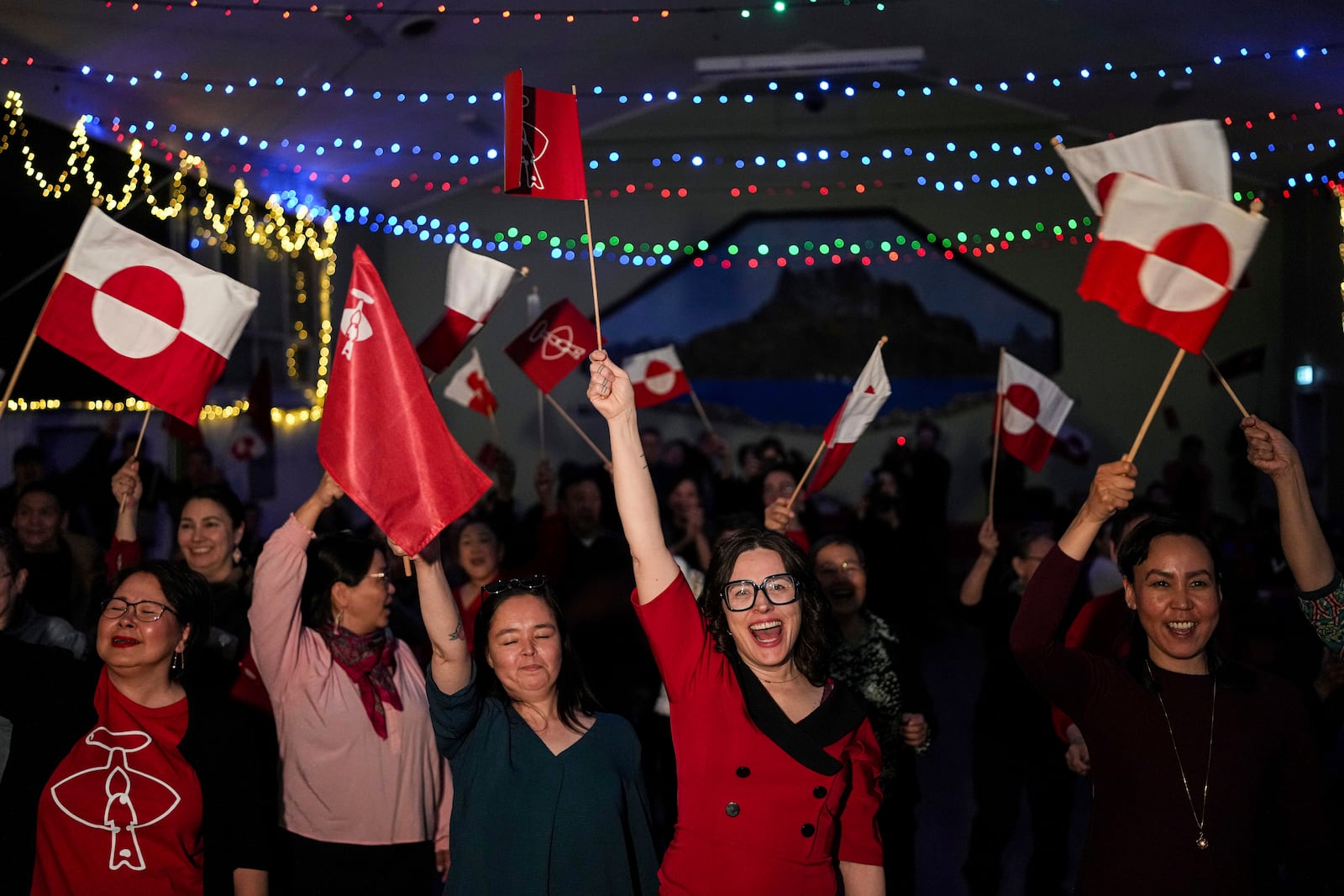 Members of Inuit Ataqatigiit political party dance with national flags at a party after parliamentary elections in Nuuk, Greenland, Tuesday, March 11, 2025. (AP Photo/Evgeniy Maloletka)