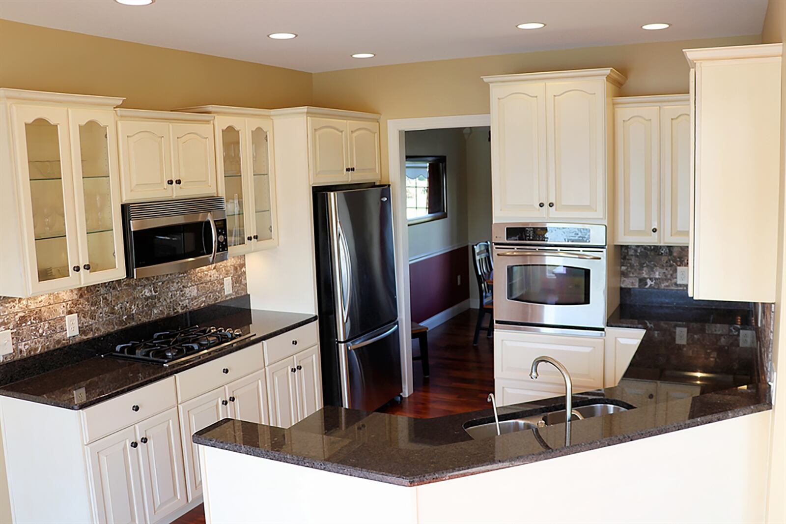 An angled peninsula counter divides the kitchen from the breakfast room. The peninsula has a dual-counter with breakfast bar seating and a double-sink within the lower counter. Dark granite countertops complement the antique white cabinetry. CONTRIBUTED PHOTO BY KATHY TYLER