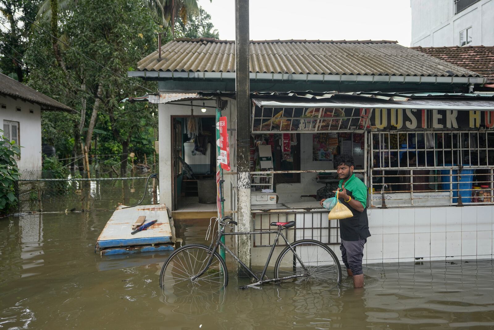 A man buys groceries in his flooded neighborhood in Colombo, Sri Lanka, Monday, Oct. 14, 2024. (AP Photo/Eranga Jayawardena)