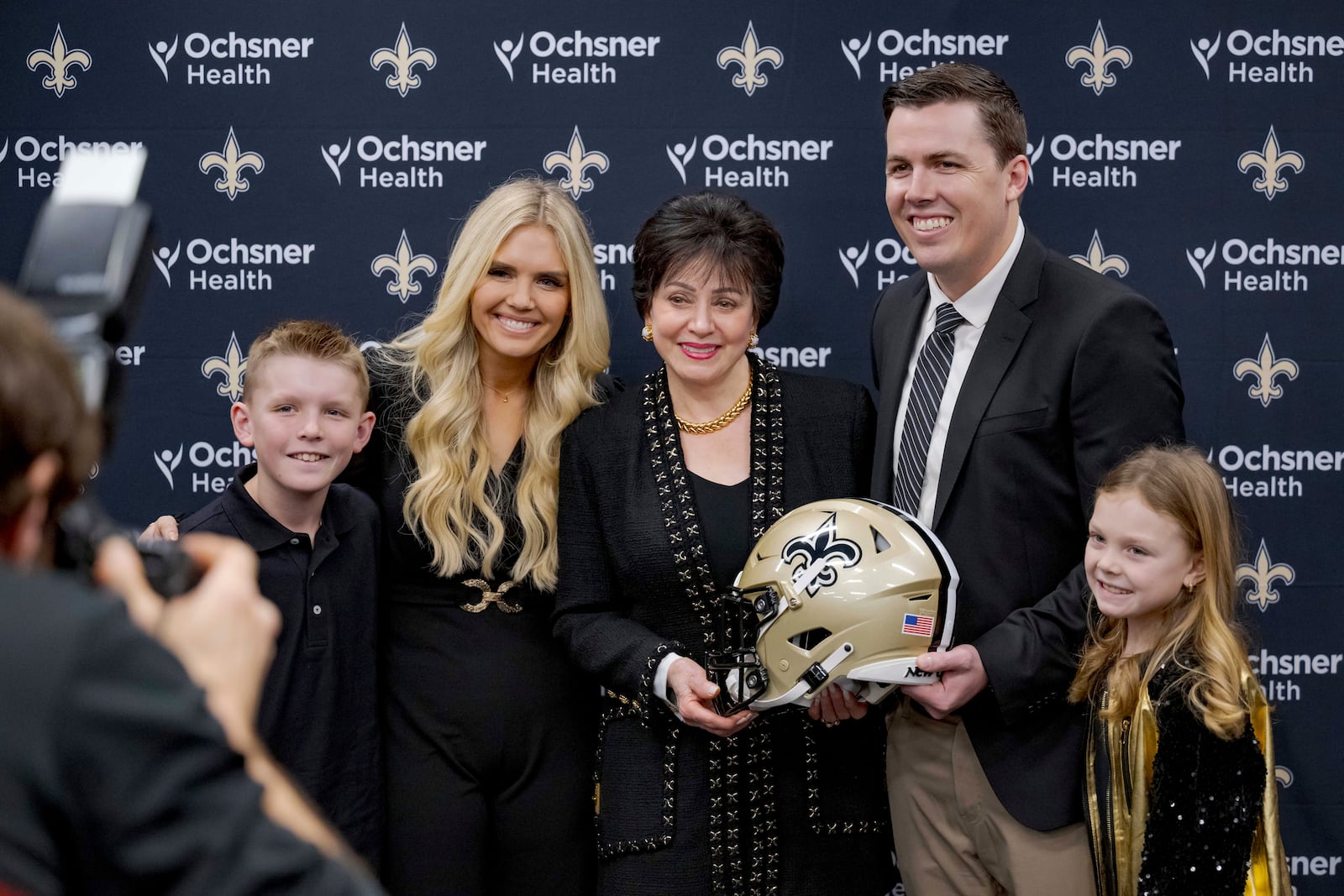 New Orlean Saints new coach Kellen Moore, Saints owner Gayle Benson, center, and Moore's son Kyler Moore, left, wife Julie Moore, and daughter Halle Moore, right, pose during an NFL football press conference in Metairie, La. Thursday, Feb. 13, 2025. (AP Photo/Matthew Hinton)