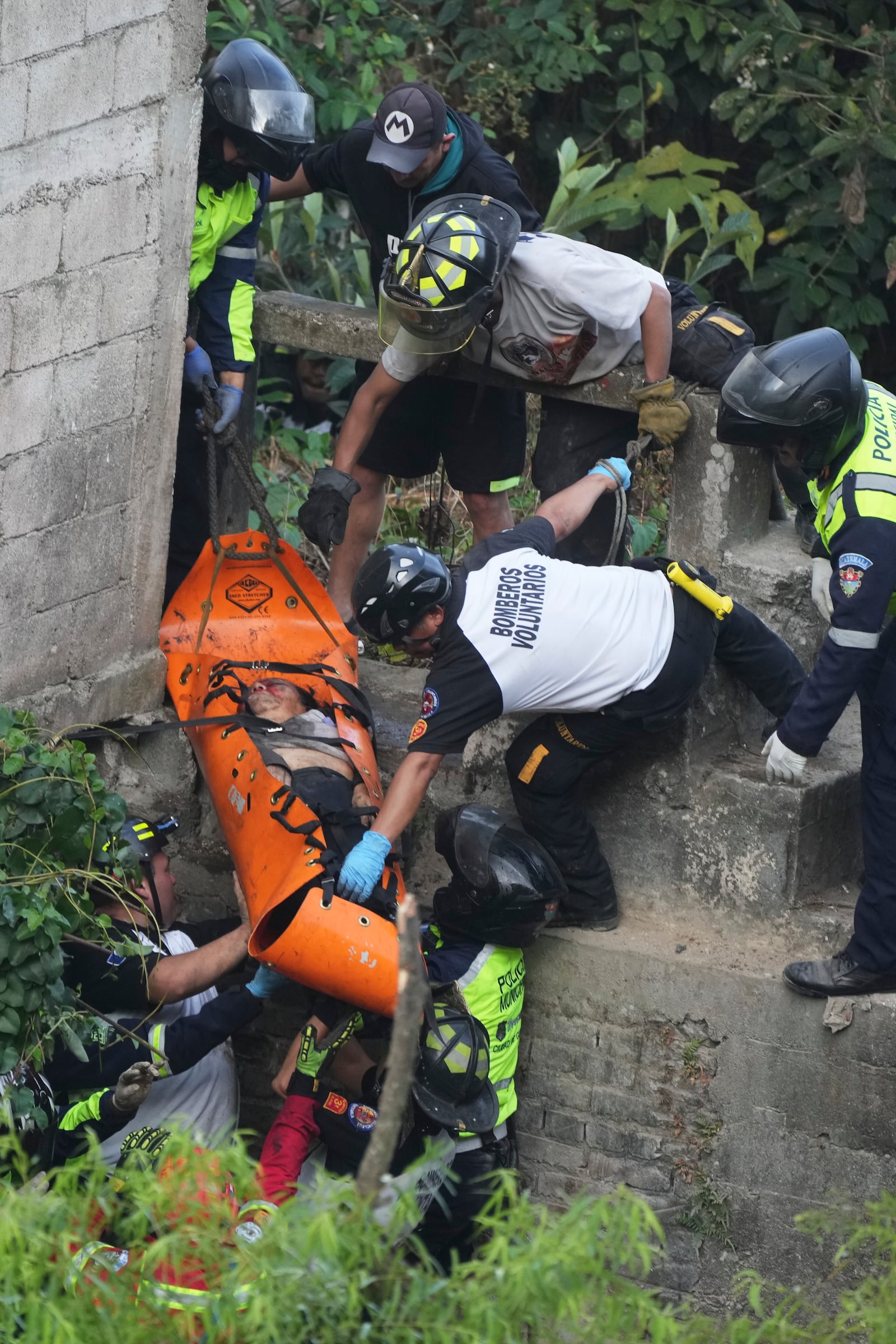 Firefighters lift a stretcher carrying a victim after a bus fell from a bridge on the outskirts of Guatemala City, Monday, Feb. 10, 2025. (AP Photo/Moises Castillo)