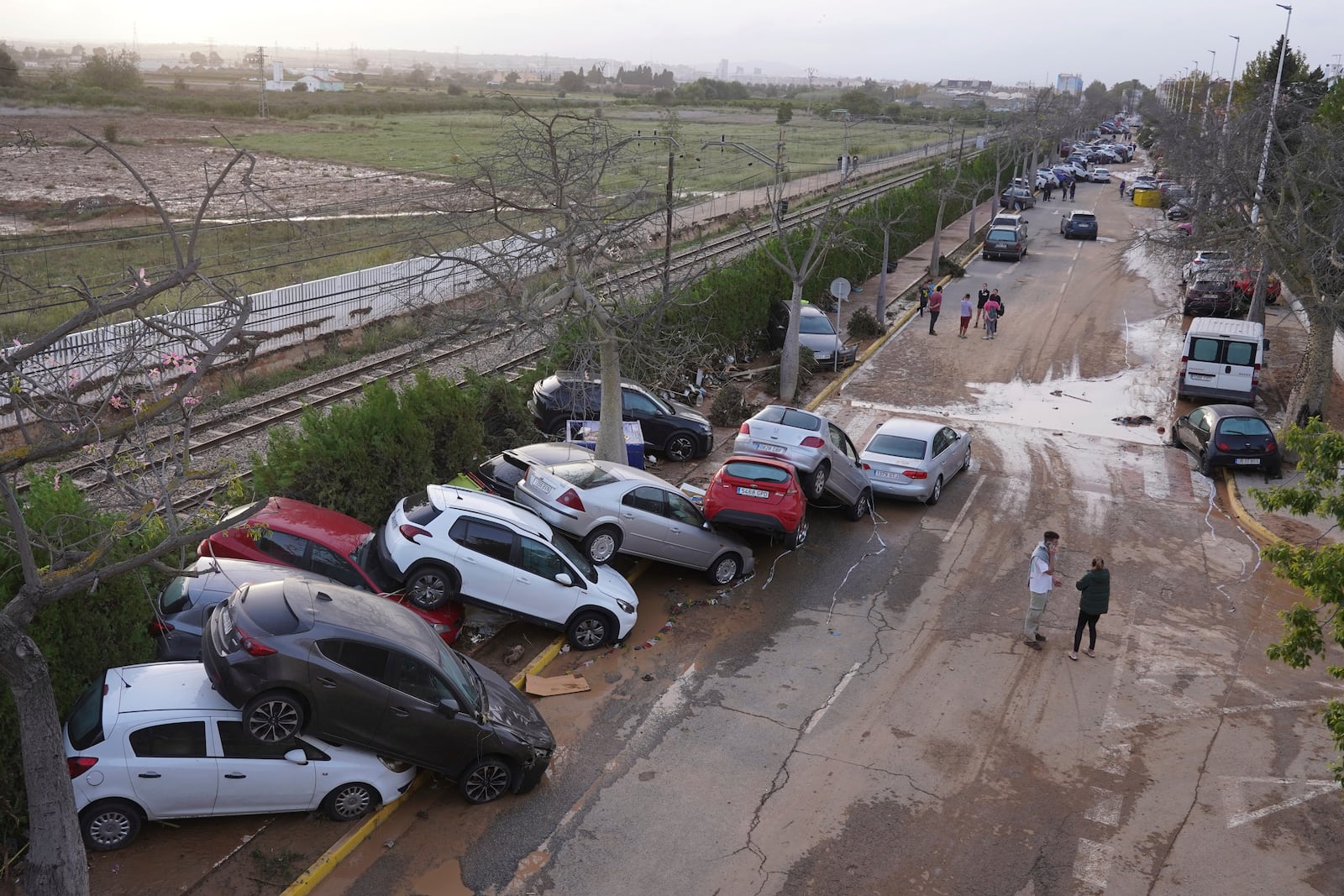 Residents walk next to cars piled up after being swept away by floods in Paiporta, near Valencia, Spain, Wednesday, Oct. 30, 2024. (AP Photo/Alberto Saiz)