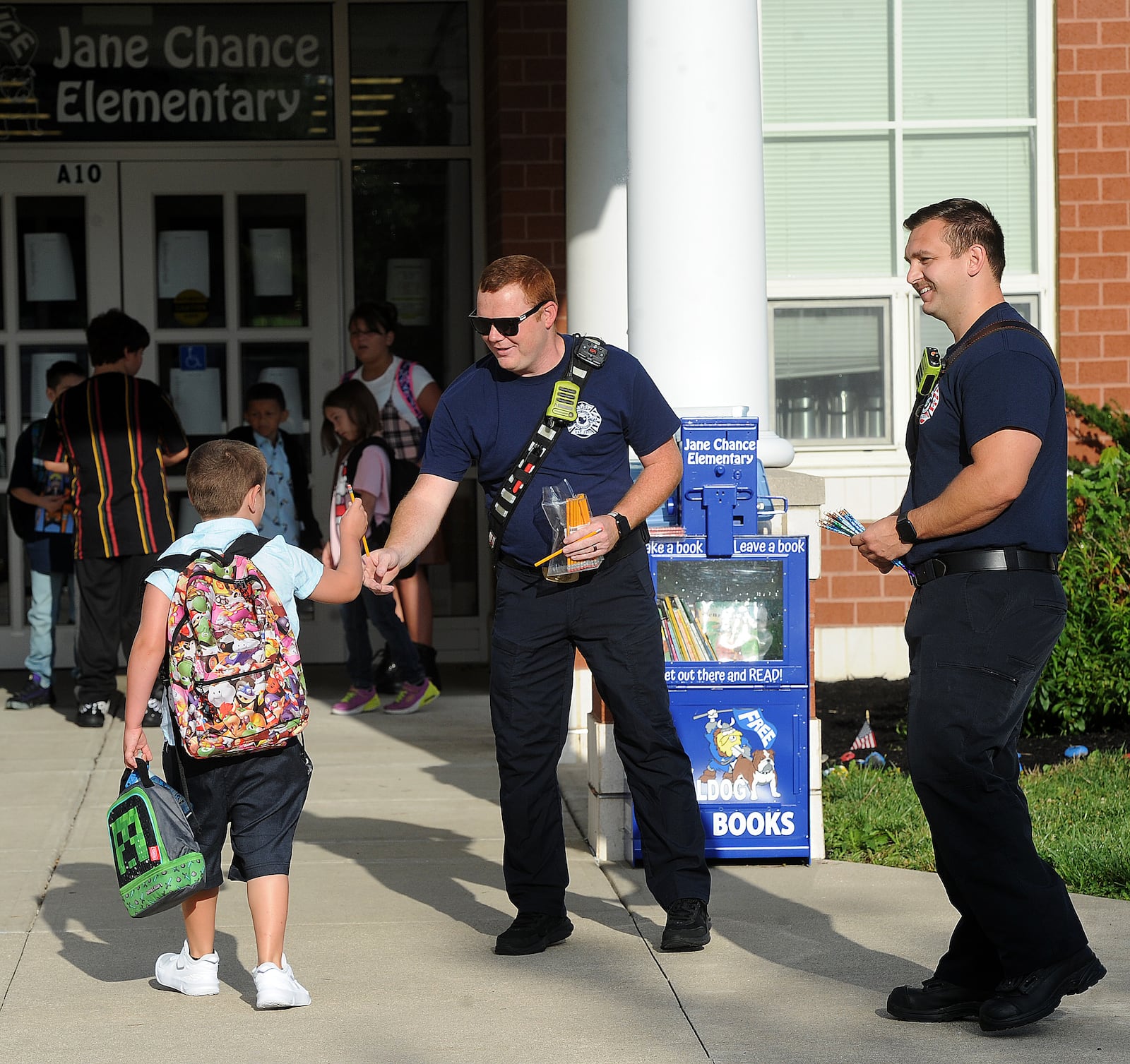 Miami Valley Fire District firefighter/Paramedics, from left,  Jerrod Widener and Caleb Young greet students with a new pencil at Jane Chance Elementary in Miamisburg, on the first day of school, Tuesday, Aug. 15, 2023. MARSHALL GORBY\STAFF