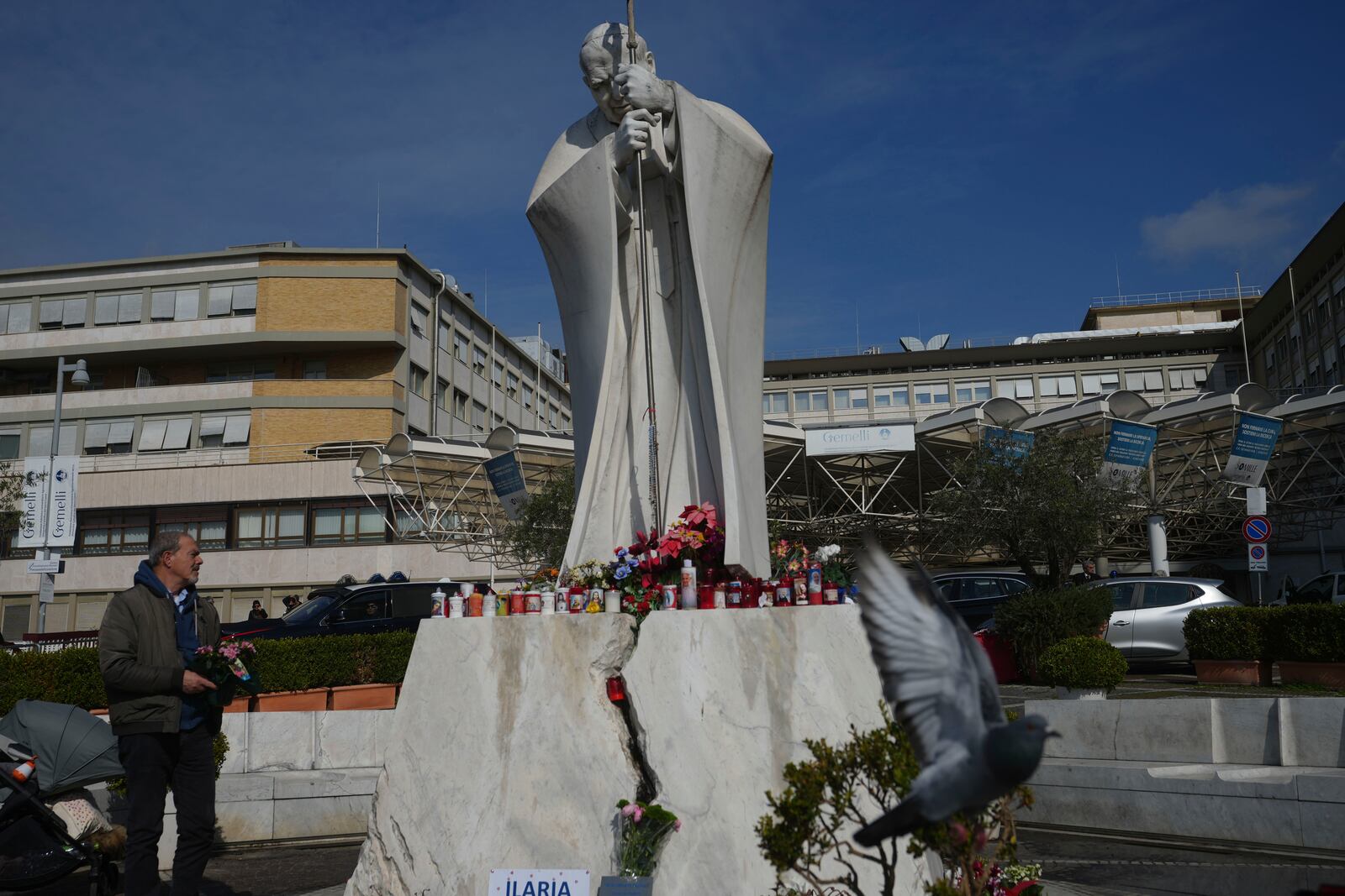 A man carries flowers at the statue of Pope John Paul II in front of the Agostino Gemelli Polyclinic, in Rome, Thursday, Feb. 20, 2025, where the Pontiff is hospitalized since Friday, Feb. 14.(AP Photo/Alessandra Tarantino)