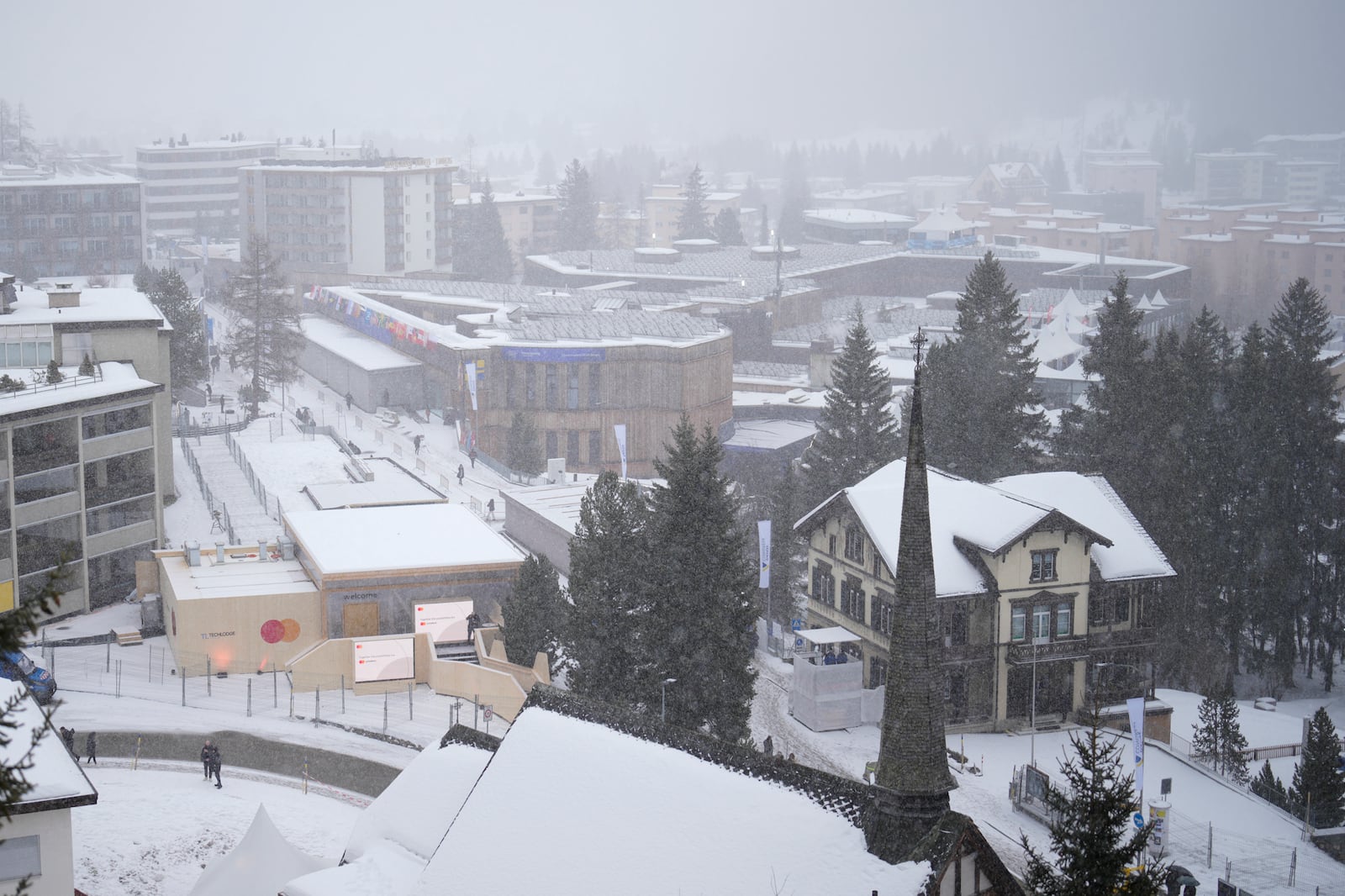 People walk during snow fall in front of the Congress Center, center, where the World Economic Forum takes place in Davos, Switzerland, Thursday, Jan. 23, 2025. (AP Photo/Markus Schreiber)