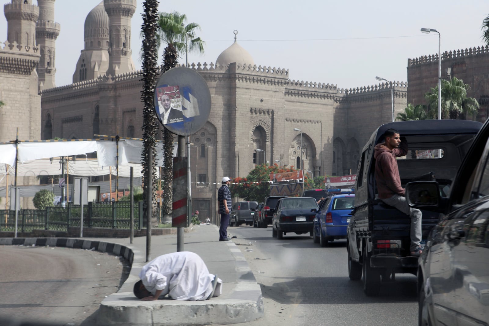 FILE - The motorcade of former U.S. President Jimmy Carter passes a man praying in the street beneath an election poster for presidential candidate Khaled Ali during the election of a new president after the fall of ex-President Hosni Mubarak in Cairo, May 23, 2012. (AP Photo/Thomas Hartwell, File)