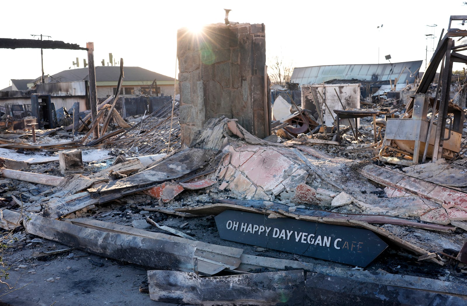 A sign for the Oh Happy Day Vegan Cafe lies in front of the destroyed restaurant after the Eaton Fire, Tuesday, Jan. 14, 2025, in Altadena, Calif. (AP Photo/Chris Pizzello)