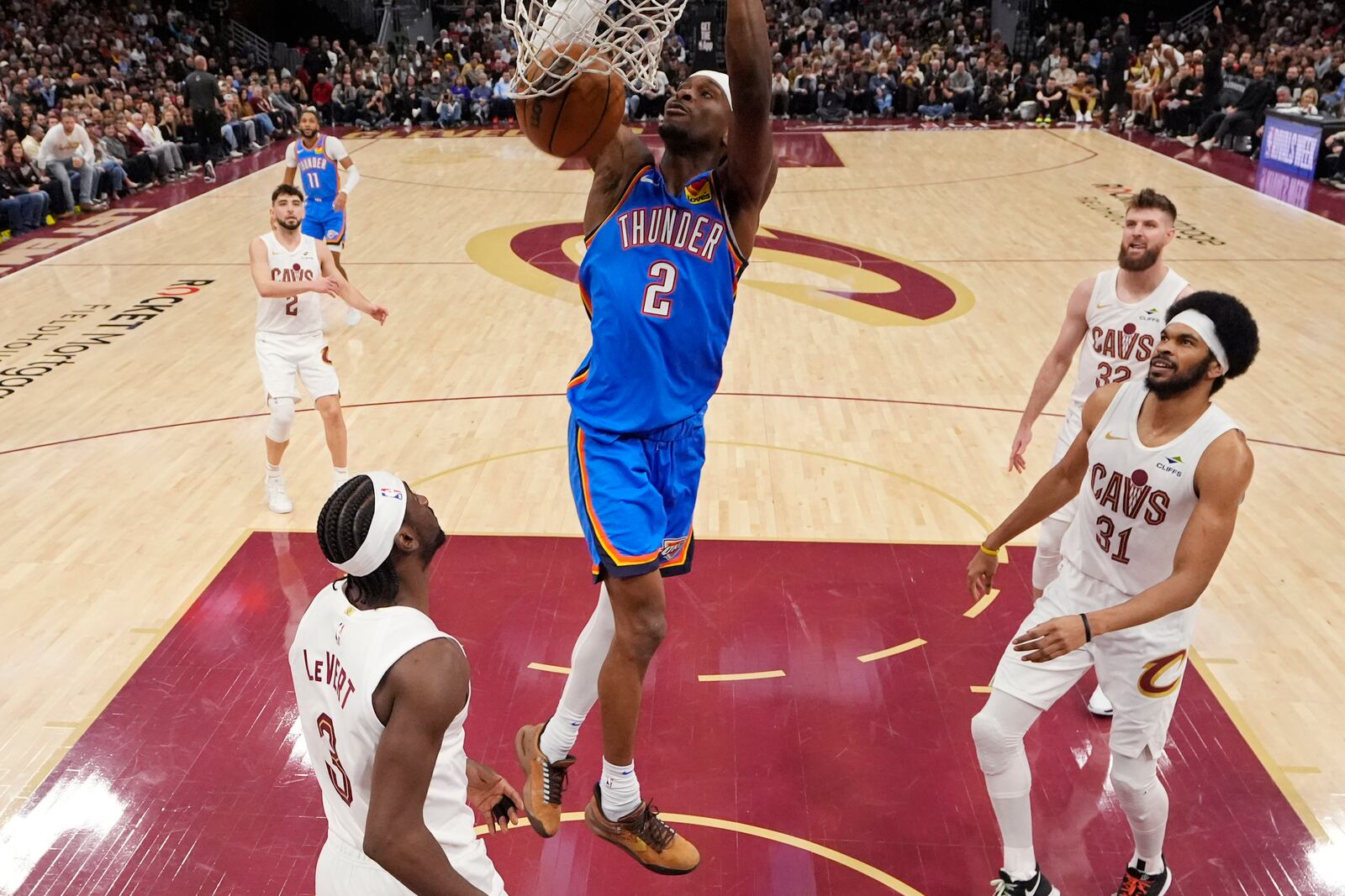 Oklahoma City Thunder guard Shai Gilgeous-Alexander (2) dunks between Cleveland Cavaliers guard Caris LeVert (3) and center Jarrett Allen (31) in the first half of an NBA basketball game, Wednesday, Jan. 8, 2025, in Cleveland. (AP Photo/Sue Ogrocki)