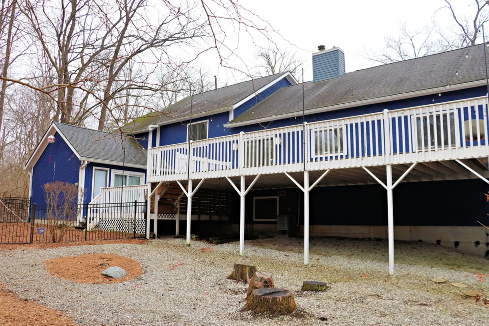 A large multi-level wooden deck stretches across the back of the house and has two sets of steps for backyard access.