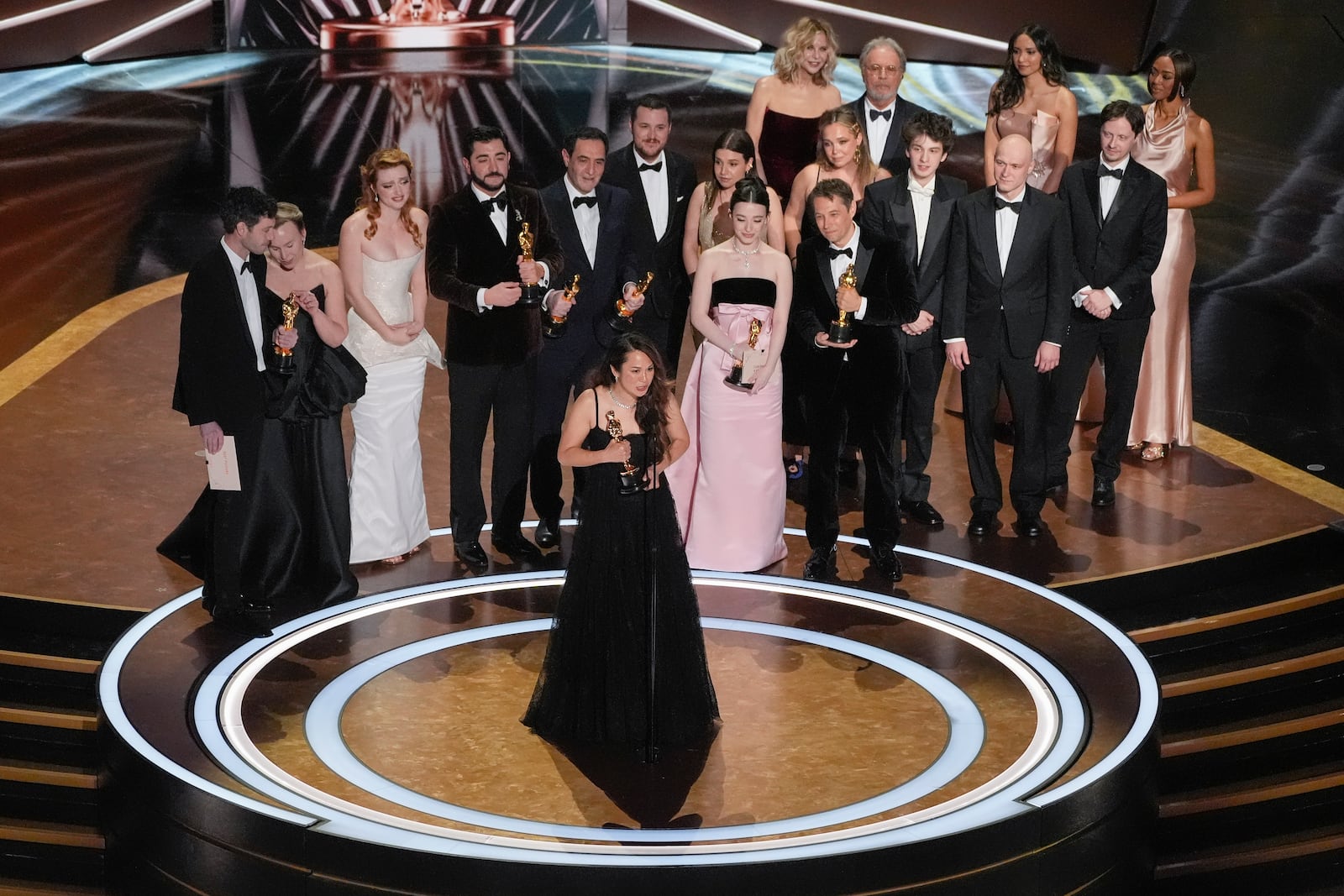 Samantha Quan, front center, accepts the award for best picture for "Anora" during the Oscars on Sunday, March 2, 2025, at the Dolby Theatre in Los Angeles. Alex Coco, from rear left, Darya Ekamasova, Lindsey Normington, Vache Tovmasyan, Karren Karagulian, Vincent Radwinsky, Luna Sofía Miranda, Mikey Madison, Sean Baker, x, Mark Eydelshteyn, Yura Borisov, Meg Ryan, and Billy Crystal look on from back. (AP Photo/Chris Pizzello)