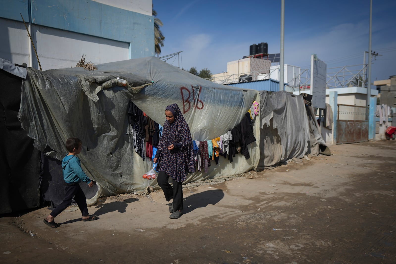 A woman and a child walk outside their tent at a camp for displaced Palestinians in Deir al-Balah, central Gaza Strip, Friday Jan. 17, 2025. (AP Photo/Abdel Kareem Hana)