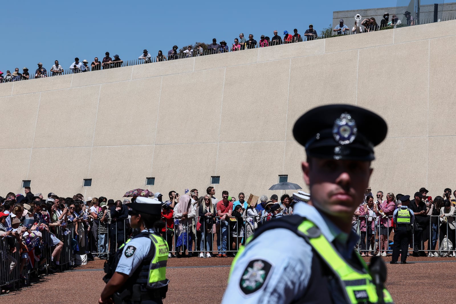 Police keep watch as people wait to see Britain's King Charles III and Queen Camilla outside Parliament House in Canberra, Australia, Monday, Oct. 21, 2024. (David Gray/Pool Photo via AP)