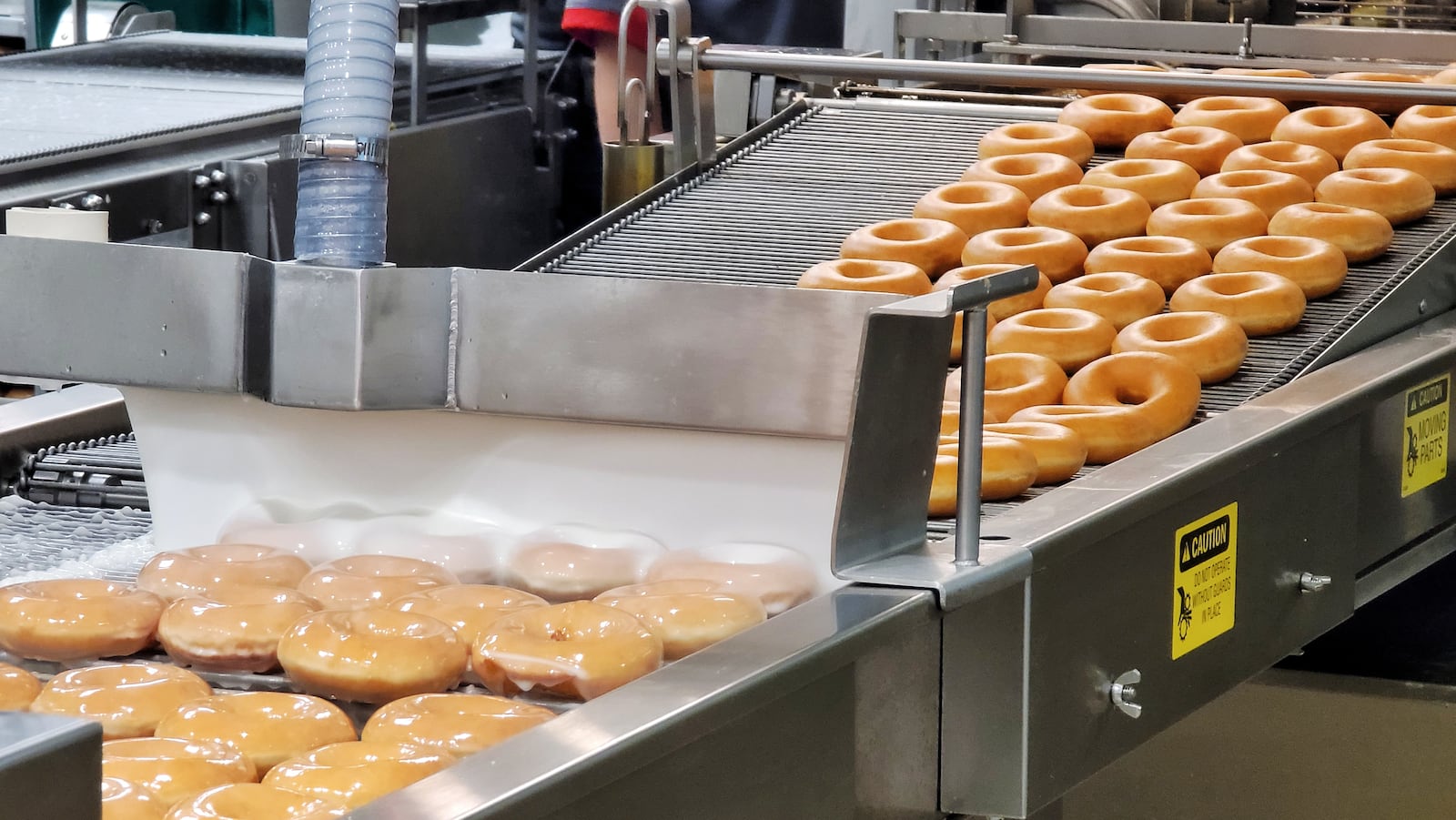 Glazed doughnuts roll down a conveyor belt Tuesday morning at Krispy Kreme, the first Butler County location. NICK GRAHAM/STAFF