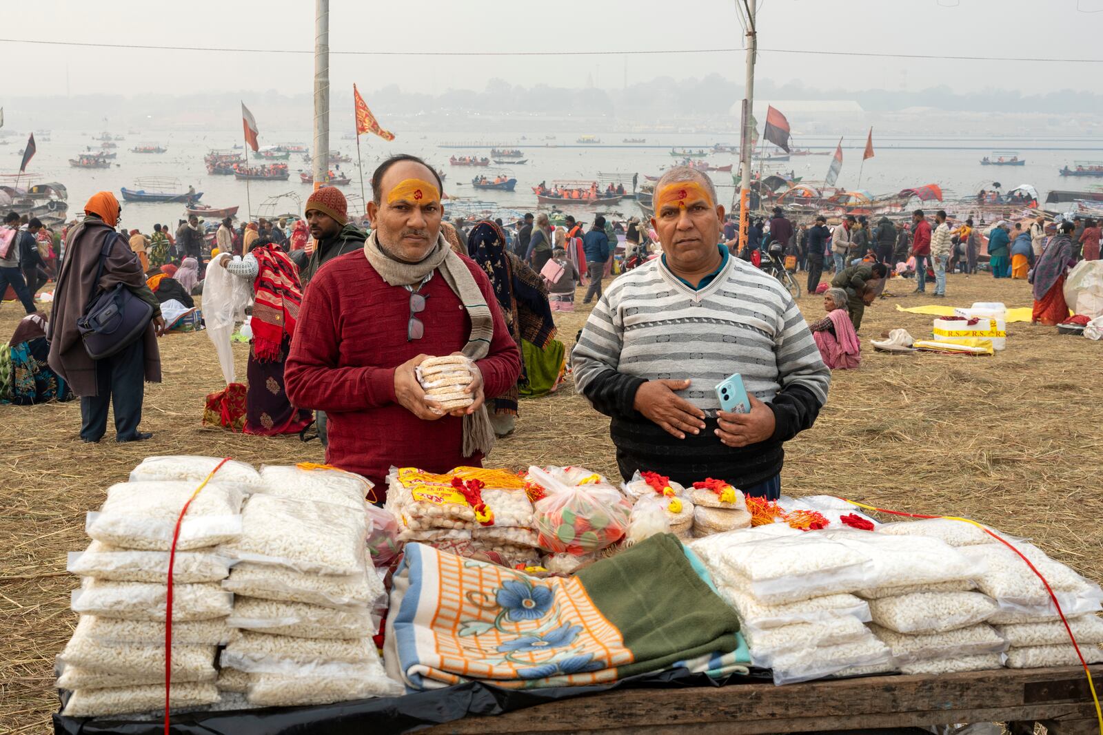 Mata Prasad Upadhyay, right, and his brother have sacred marks reading 'Om' stamped in vermillion on their foreheads as they buy snacks after bathing at the confluence of the Ganges, the Yamuna, and the Saraswati rivers the day before the 45-day-long Maha Kumbh festival in Prayagraj, India, Sunday, Jan. 12, 2025. (AP Photo/Ashwini Bhatia)