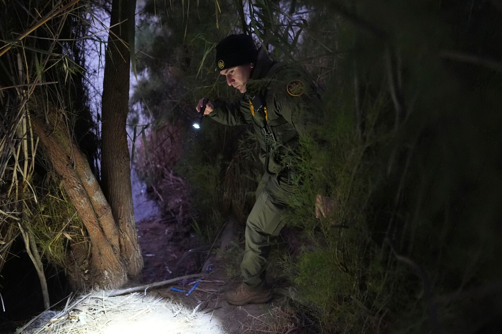 A border patrol agent walks along a trail littered with bracelets used by human smuggling groups near the Rio Grande at the U.S.-Mexico border, Thursday, Feb. 13, 2025, in McAllen, Texas. (AP Photo/Eric Gay)