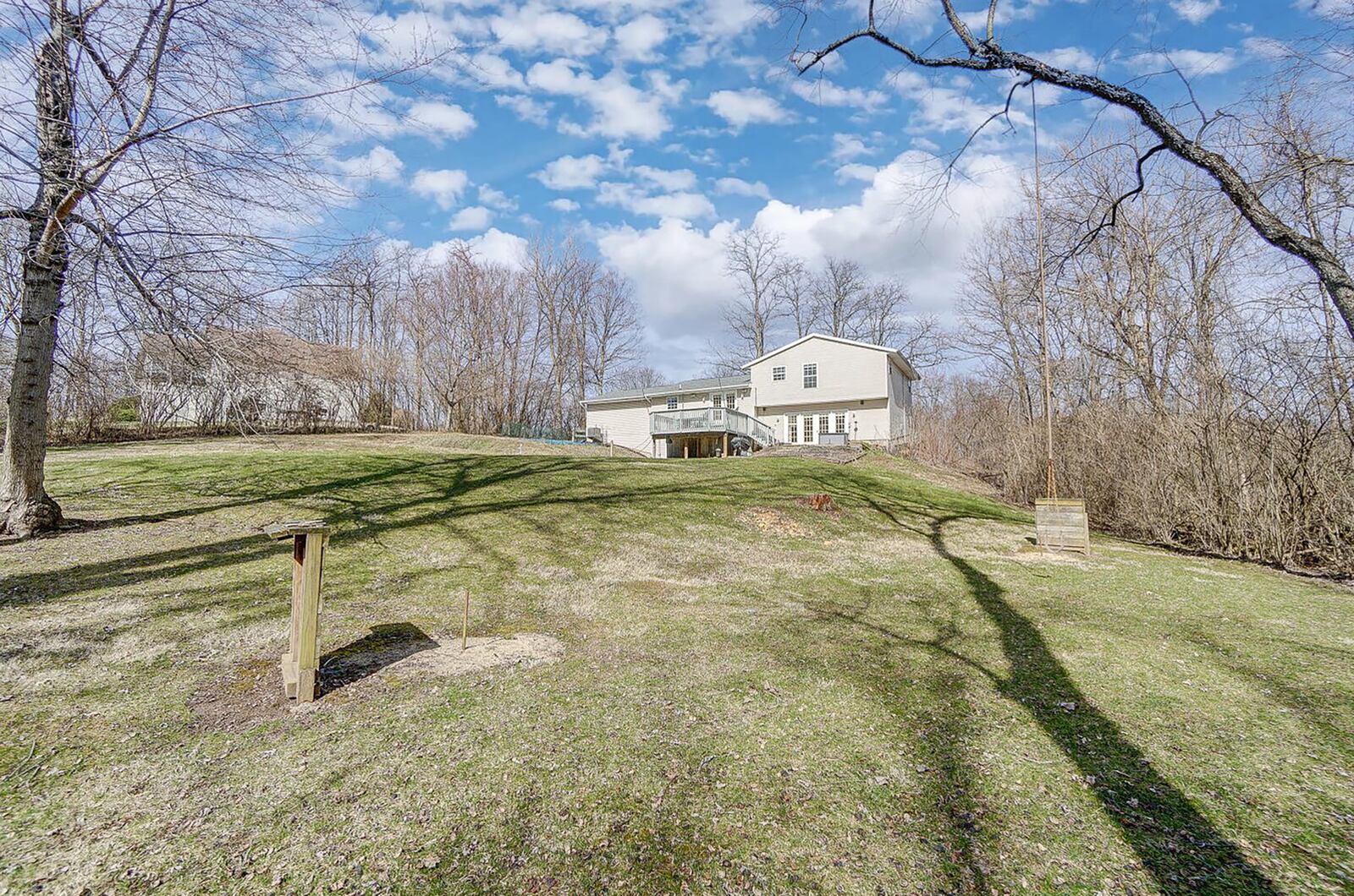 The rear of the home has a wood elevated deck, paver patio and a large rear yard with trees and rolling hills.