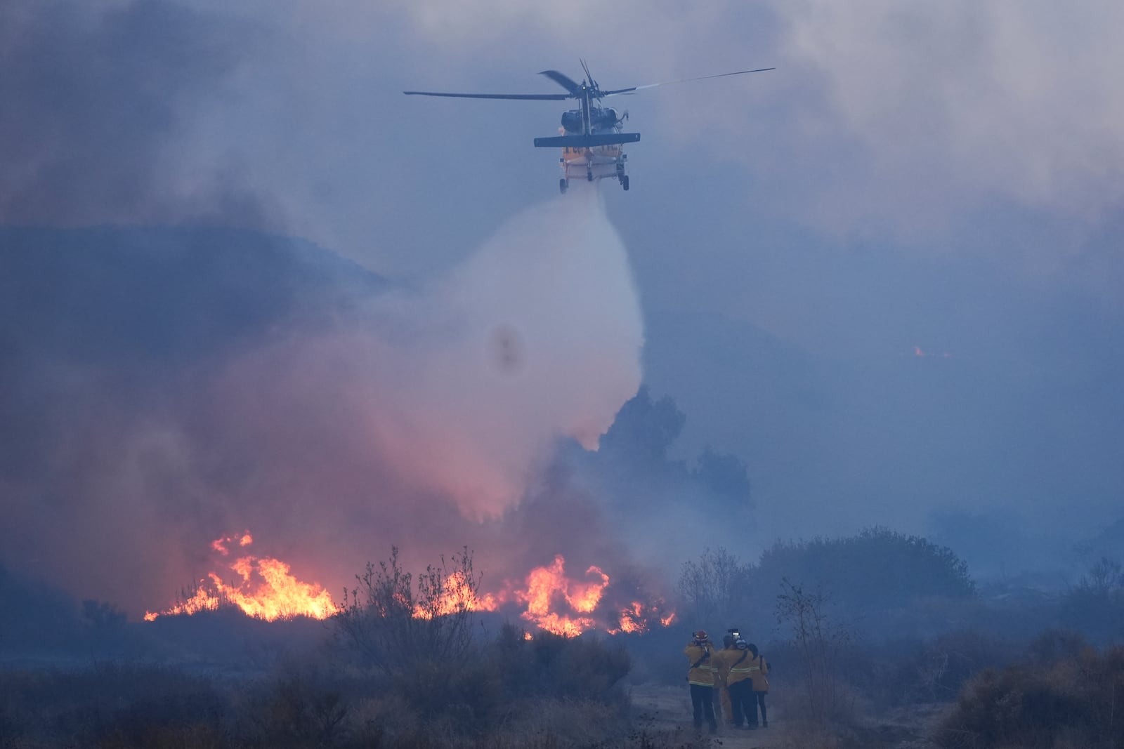 A helicopter drops water on the Hughes Fire as firefighters monitor flames in Castaic, Calif., Wednesday, Jan. 22, 2025.(AP Photo/Marcio Jose Sanchez)