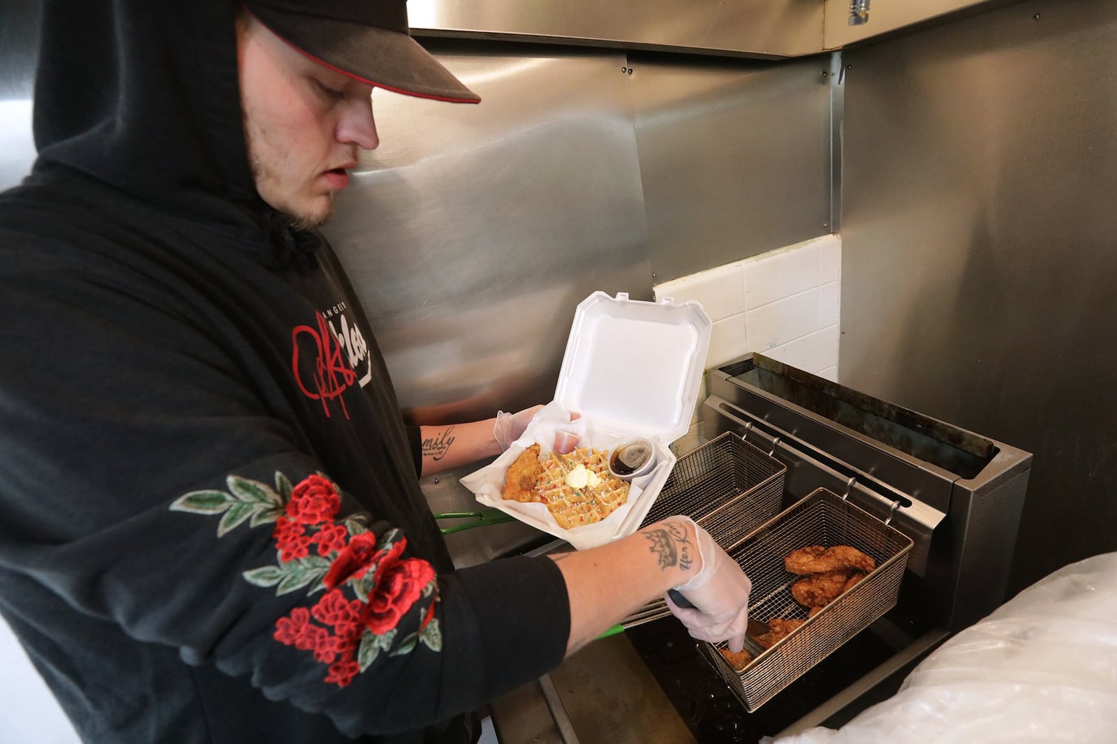 Tyler Ulmer, an employee of Bubby’s Chicken & Waffles, pulls fried chicken out of the deep fryer in the community kitchen on the lower level of the Bushnell Building. BILL LACKEY/STAFF