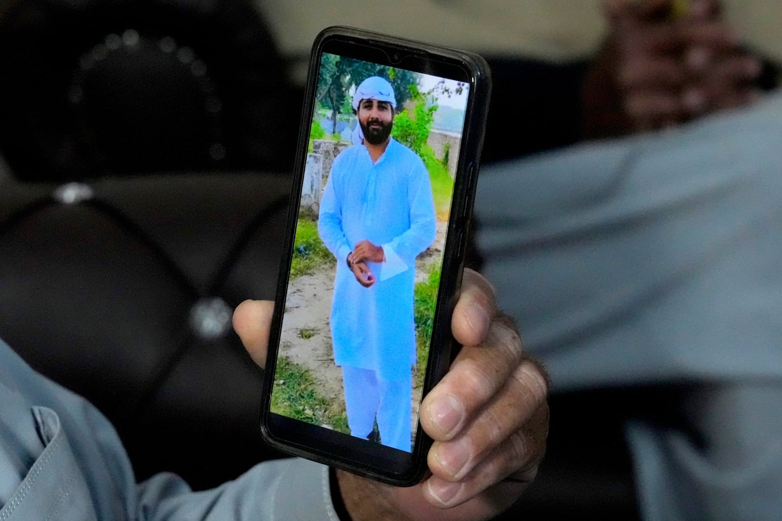 A Pakistani Mohammad Akram shows a picture of his son Abu Bakar, one of the victims of a migrant boat that capsized in West Africa's Atlantic coastline, on his cell phone at his home, in Jura village, in the Lalamusa district in Pakistan, Friday, Jan. 17, 2024. (AP Photo/K.M. Chaudary)