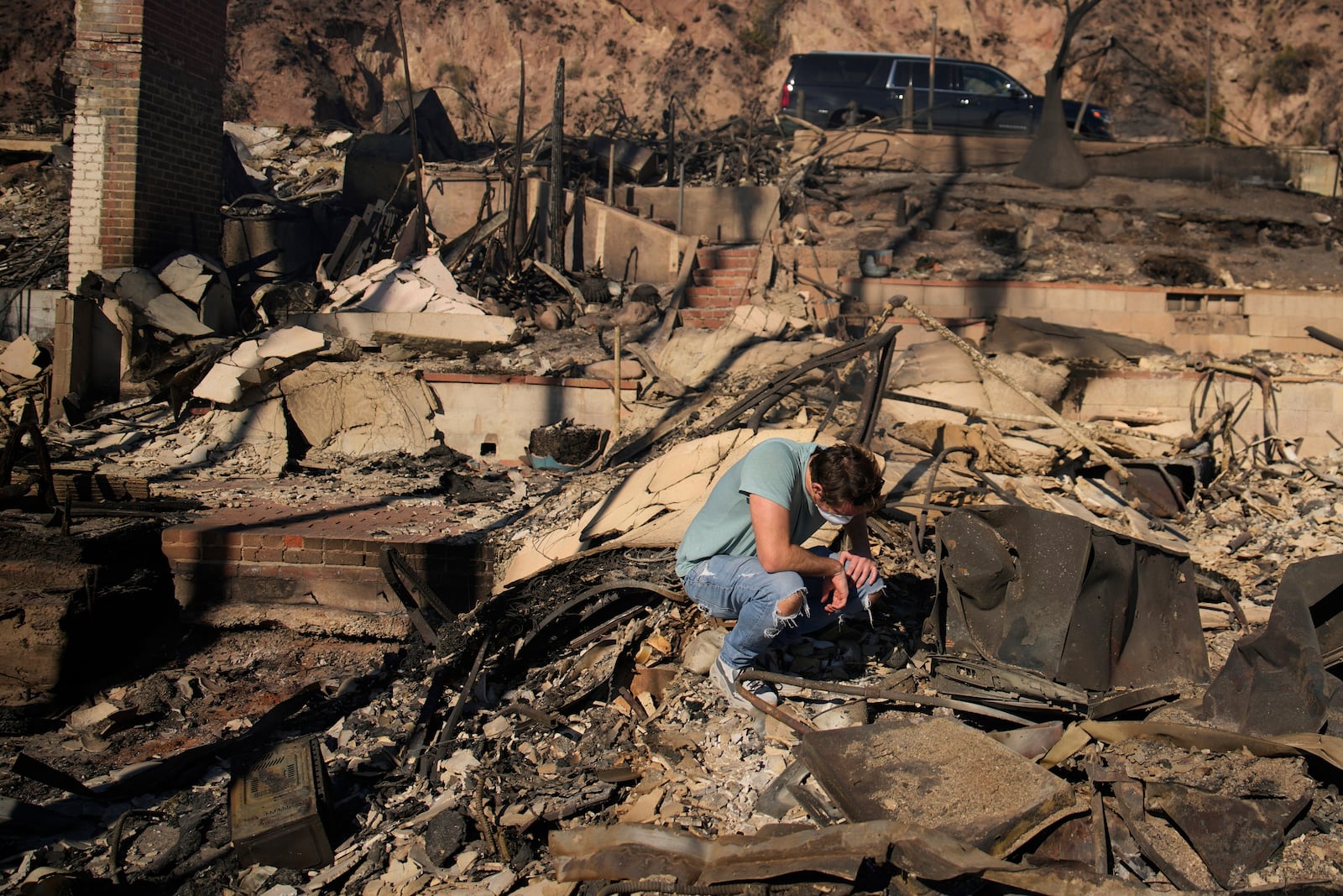 Luke Dexter kneels as he sifts through the remains of his father's fire-ravaged beach front property in the aftermath of the Palisades Fire on Friday, Jan. 10, 2025, in Malibu, Calif. (AP Photo/John Locher)