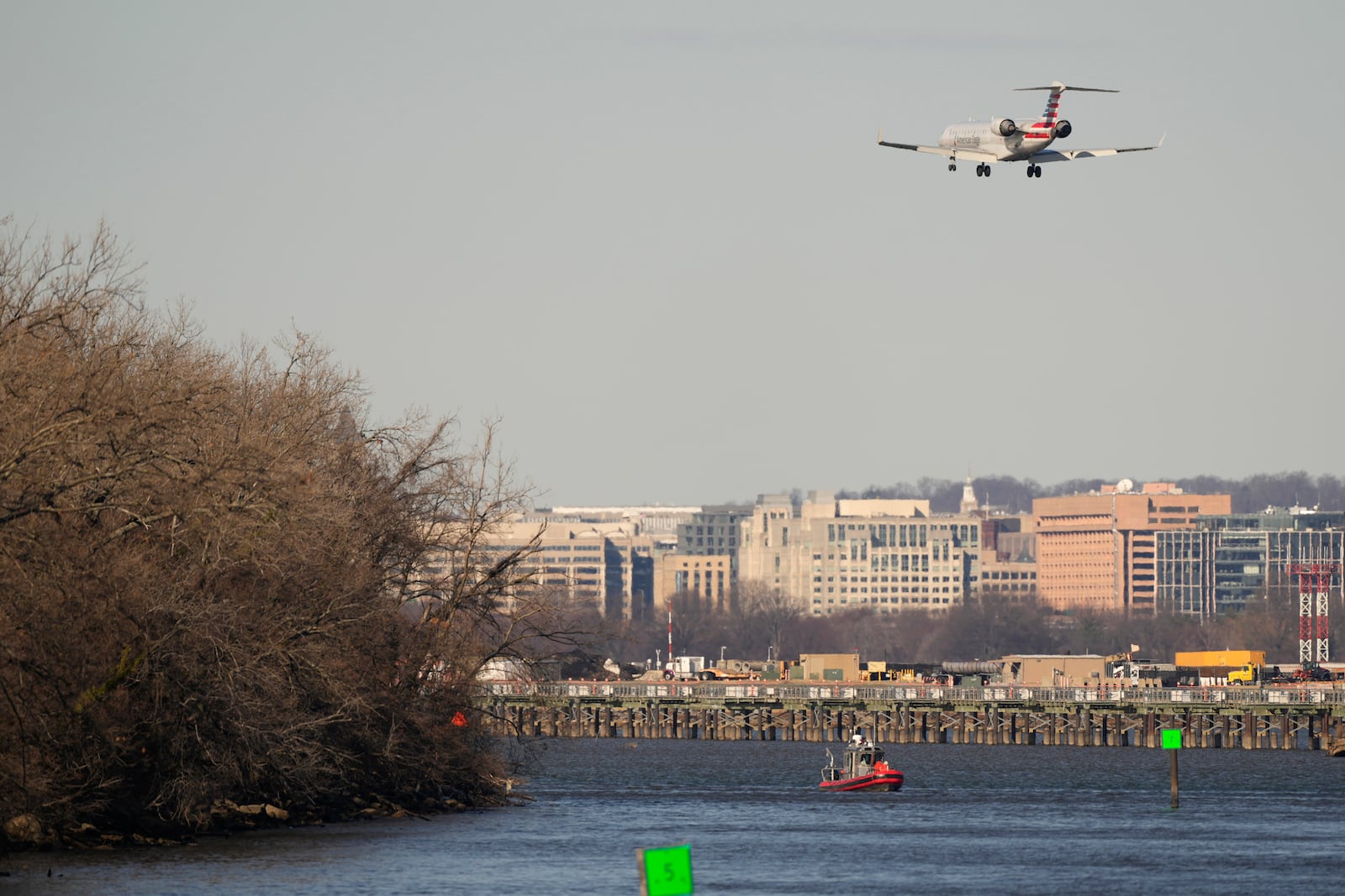 A Coast Guard boat works in the Potomac river as an American Airlines jet approaches Ronald Reagan Washington National Airport Saturday, Feb. 1, 2025, in Arlington, Va., near the wreckage site where an American Airlines jet and a Black Hawk helicopter collided, as seen from Alexandria, Va. (AP Photo/Carolyn Kaster)