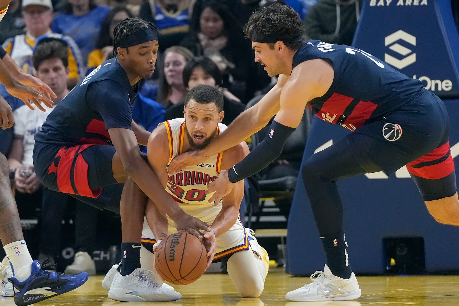 Golden State Warriors guard Stephen Curry, middle, looks to pass the ball between Washington Wizards guard Bilal Coulibaly, left, and forward Corey Kispert during the first half of an NBA basketball game in San Francisco, Saturday, Jan. 18, 2025. (AP Photo/Jeff Chiu)