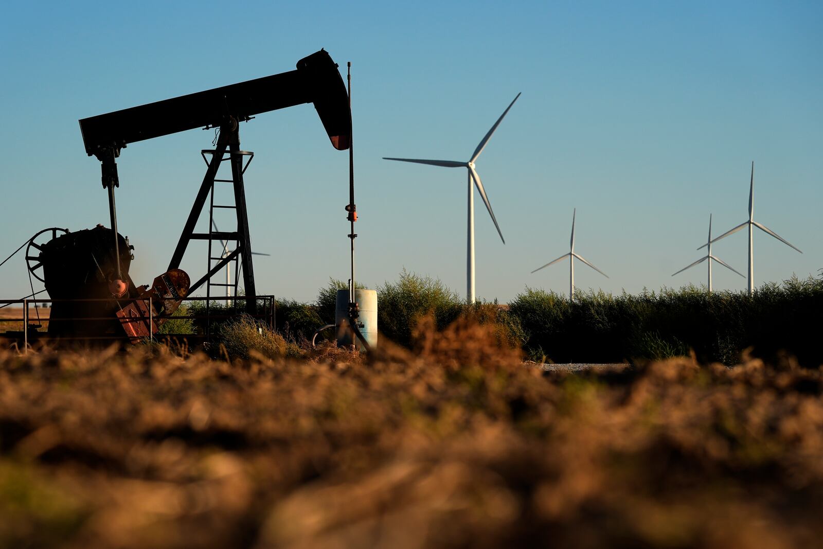 FILE - Pumpjacks operate in the foreground while wind turbines at the Buckeye Wind Energy wind farm rise in the distance, Sept. 30, 2024, near Hays, Kan. (AP Photo/Charlie Riedel, File)