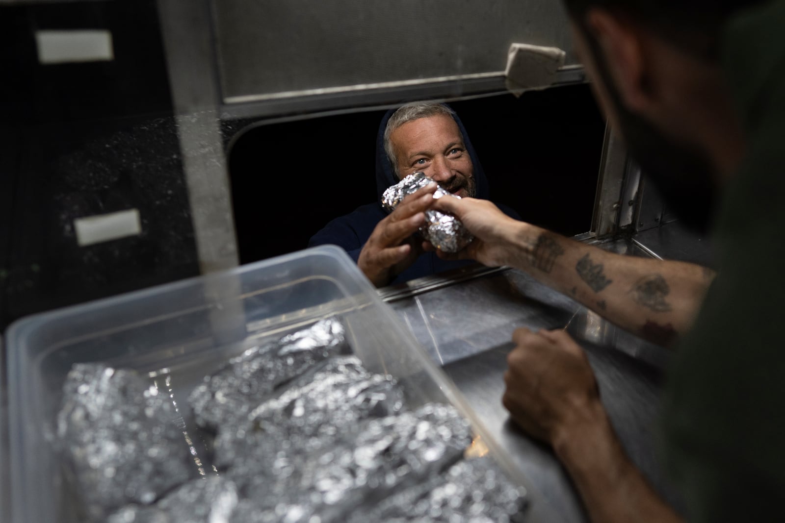 World Central Kitchen Chef Corp member Daniel Shemtob hands a burrito to an Eaton Fire first responder as he works his food truck, The Lime Truck, at the Rose Bowl Stadium, Wednesday, Jan. 15, 2025, in Pasadena, Calif. (AP Photo/Carolyn Kaster)