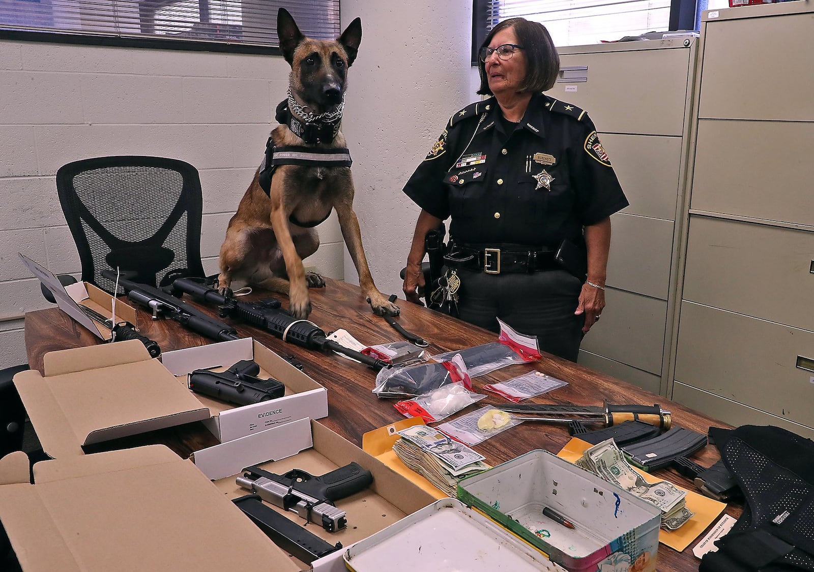 Clark County Sheriff Deb Burchett and K-9 officer Pablo with some of the items found during the search of a residence at the Belmont Apartment in Springfield Tuesday morning. Pablo was instrumental in finding the drugs and weapons in the apartment. Some of the items found were cocaine, stolen weapons, body armour and a large amount of cash. BILL LACKEY/STAFF