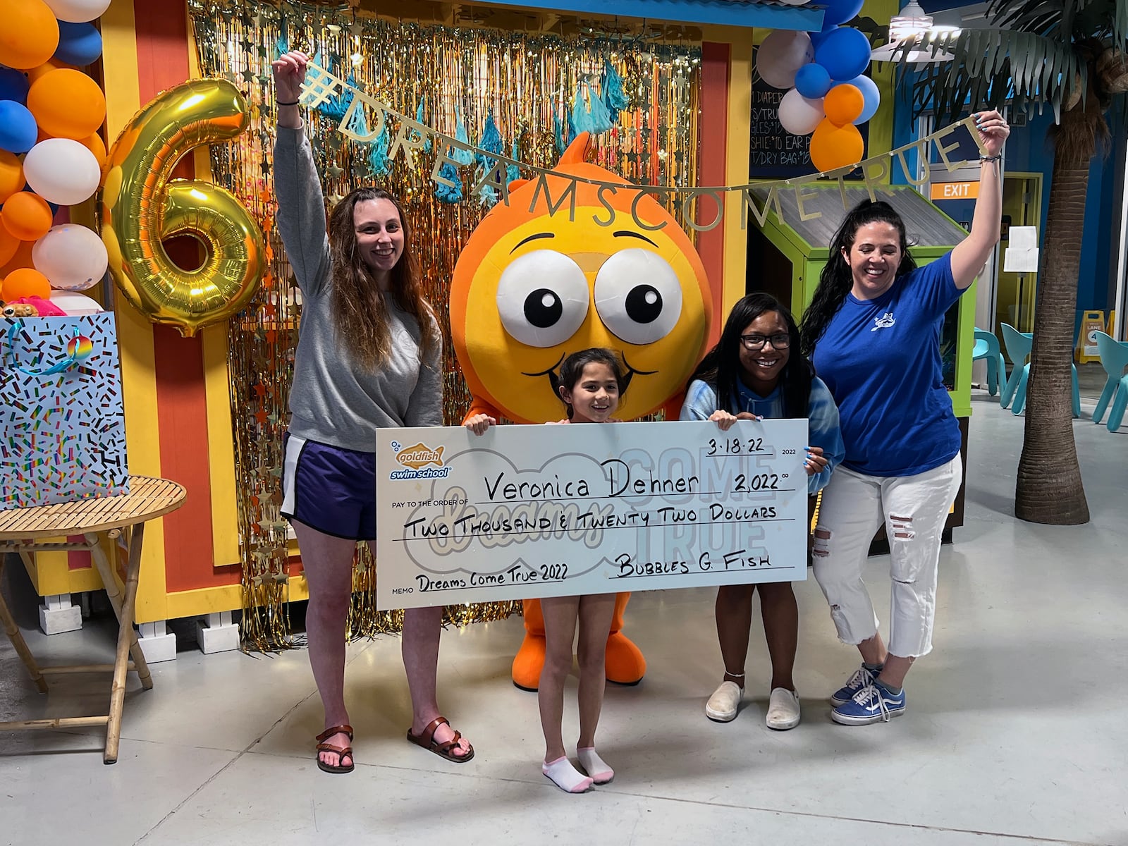 Veronica Dehner, 8, holds a giant ceremonial check, representing her prize of $2,022 from the national Goldfish Swim School franchise. She is shown with (L-R) staff members Jaden Pennix, Ryanne Hood and local Goldfish Swim School owner, Amy Strozier. Also on hand for the celebration was Bubbles G. Fish, the school's mascot. CONTRIBUTED