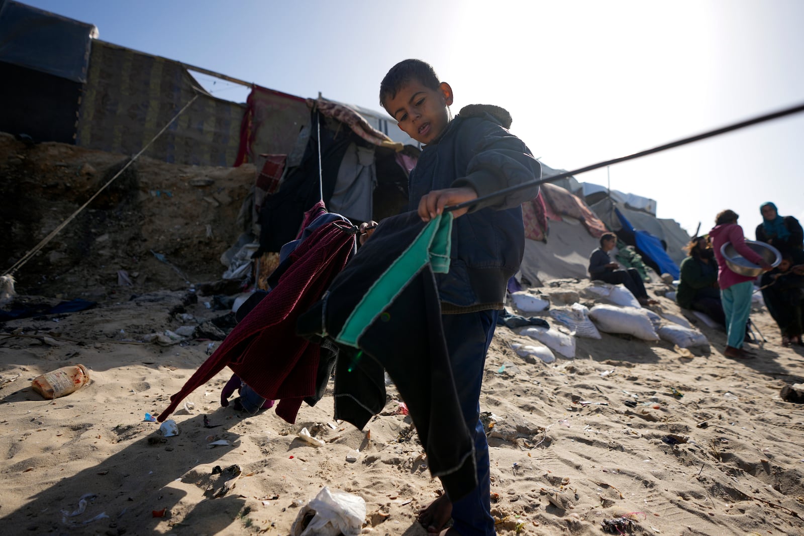 A Palestinian child hanging cloths on a rope outside tents made locally from pieces of cloth and nylon, in a camp for internally displaced Palestinians at the beachfront in Deir al-Balah, central Gaza Strip, Friday, Dec. 27, 2024. (AP Photo/Abdel Kareem Hana)