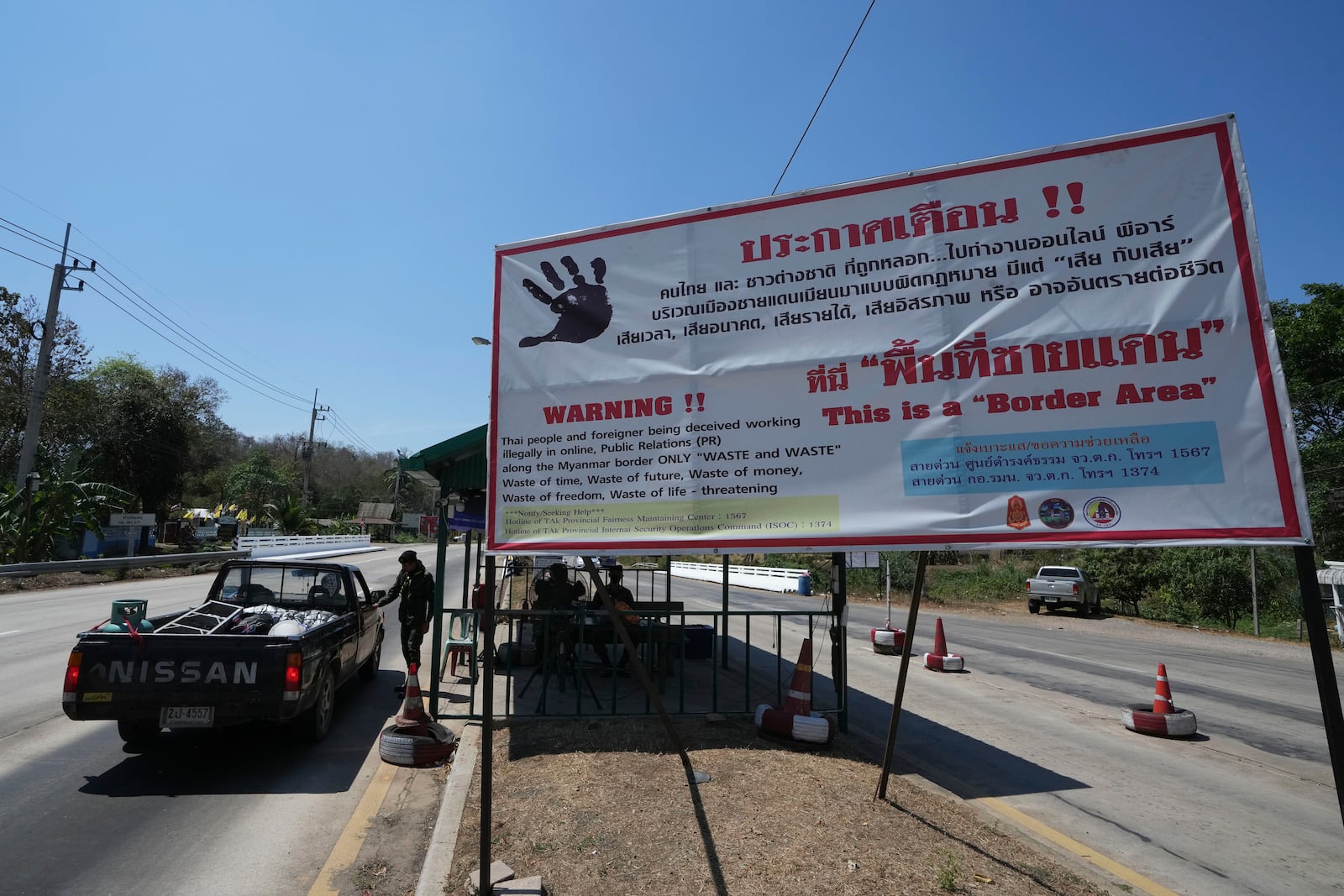 A truck pass through a military check point near display vinyl signs in Thai, English warning Thais and foreigners of the risk of being trafficked to work along the Myanmar border in Mae Sot, Tak province Wednesday, Feb. 26, 2025, (AP Photo/Sakchai Lalit)