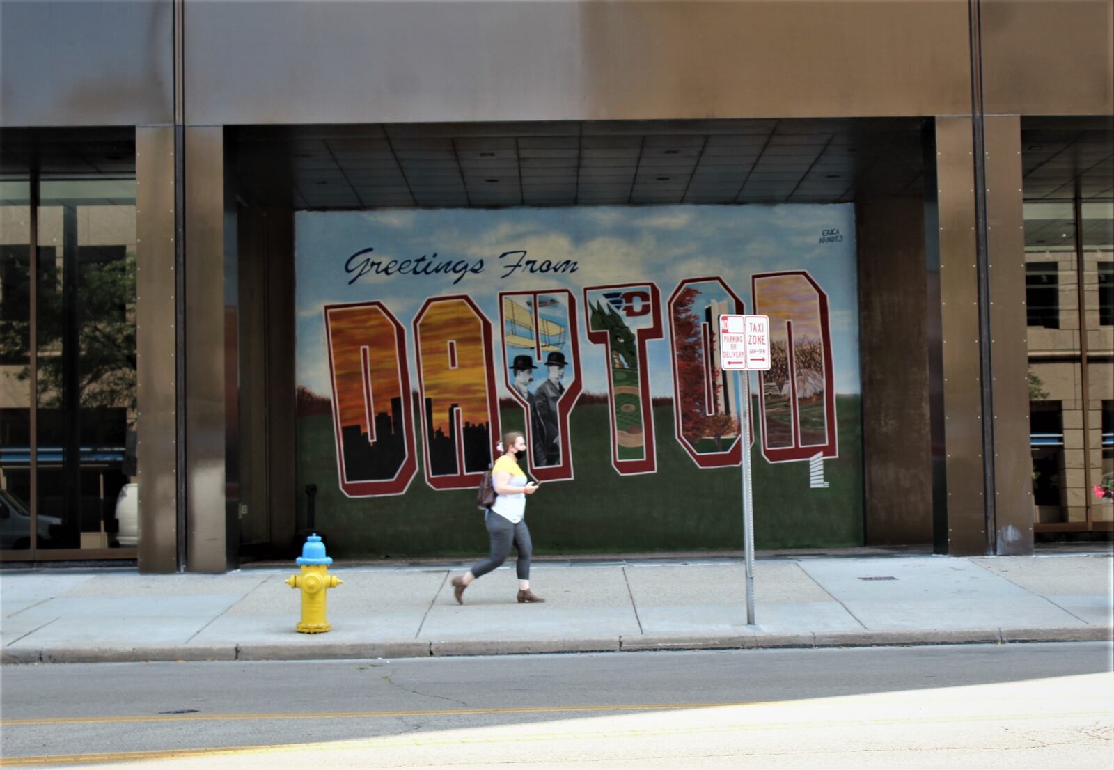 A woman on her cell phone walks past a Dayton mural in downtown. CORNELIUS FROLIK / STAFF