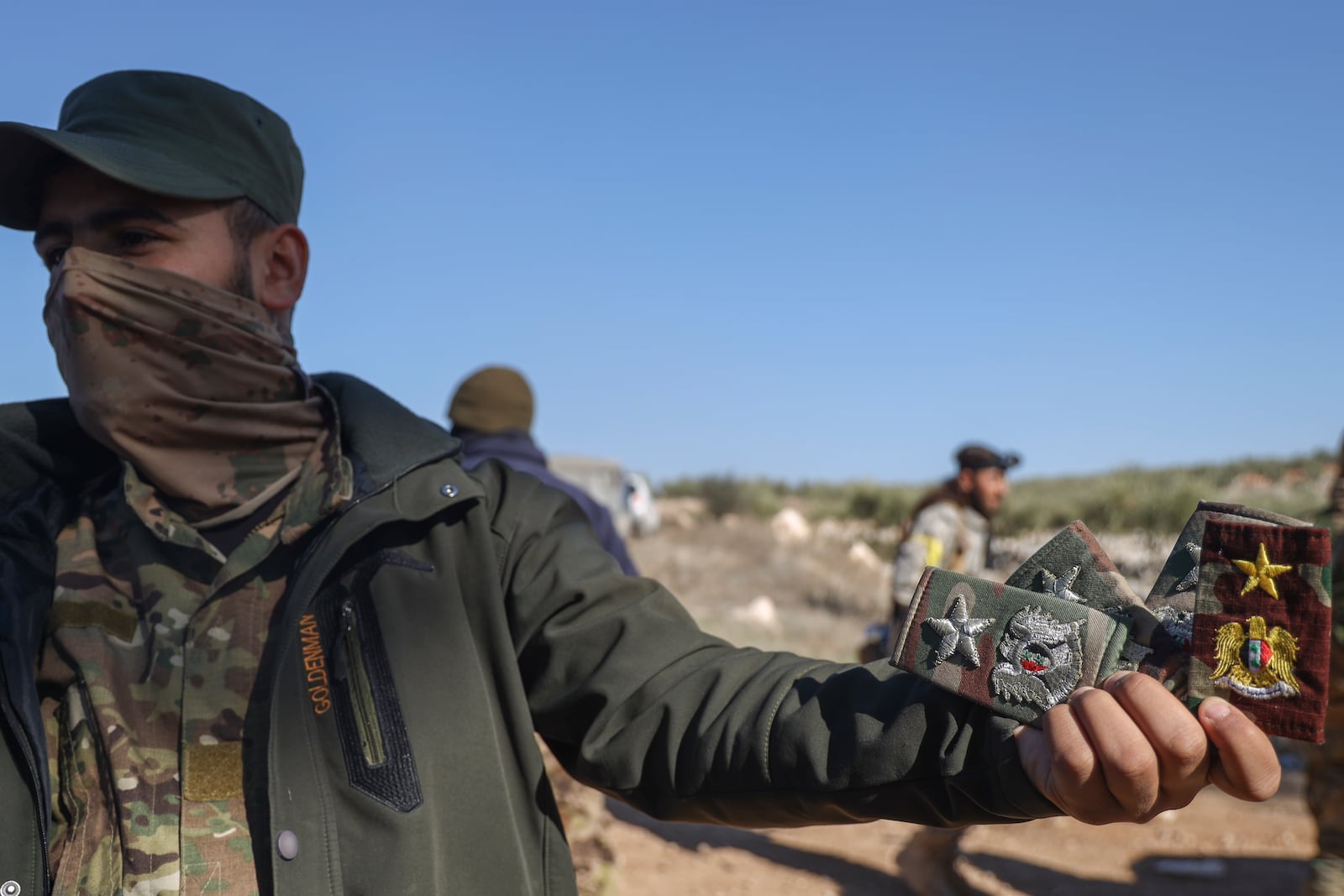 An opposition fighter displays badges belonging to Syrian army officers uniforms in Anjara, western outskirts of Aleppo, Syria, Thursday Nov. 29, 2024. Syrian armed groups launched a large-scale attack on areas controlled by government forces and seized territory in northwestern Syria, opposition groups said Thursday.(AP Photo/Omar Albam)