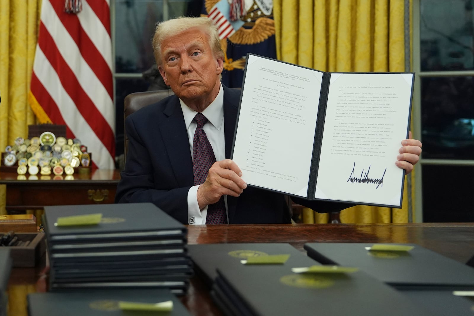 President Donald Trump holds up an executive order commuting sentences for people convicted of Jan. 6 offenses in the Oval Office of the White House, Monday, Jan. 20, 2025, in Washington. (AP Photo/Evan Vucci)