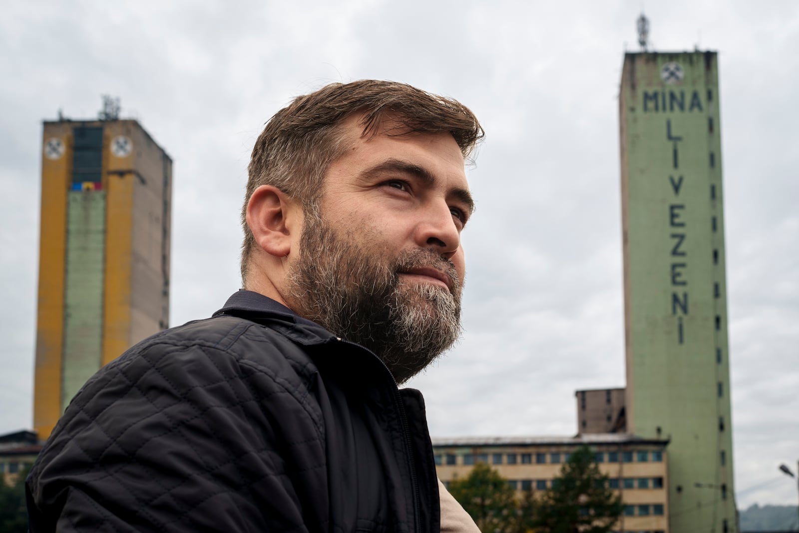 Sebastian Tirintica stands backdropped by buildings at the entrance of the Livezeni coal mine, his former workplace, in Petrosani, southern Romania, Friday, Oct. 11, 2024. (AP Photo/Vadim Ghirda)