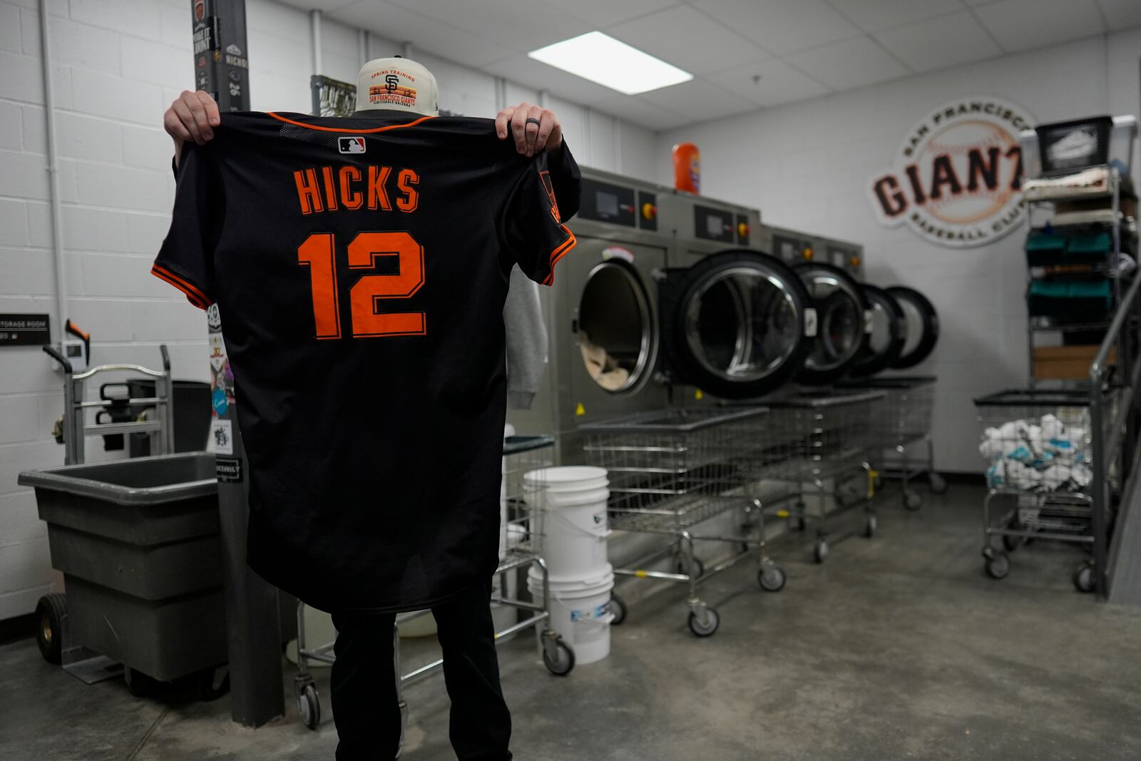 San Francisco Giants clubhouse attendant Riley Halpin inspects pitcher Jordan Hicks' jersey before putting it in the washing machine during baseball spring training at the team's facility, Monday, Feb. 17, 2025, in Scottsdale, Ariz. (AP Photo/Carolyn Kaster)