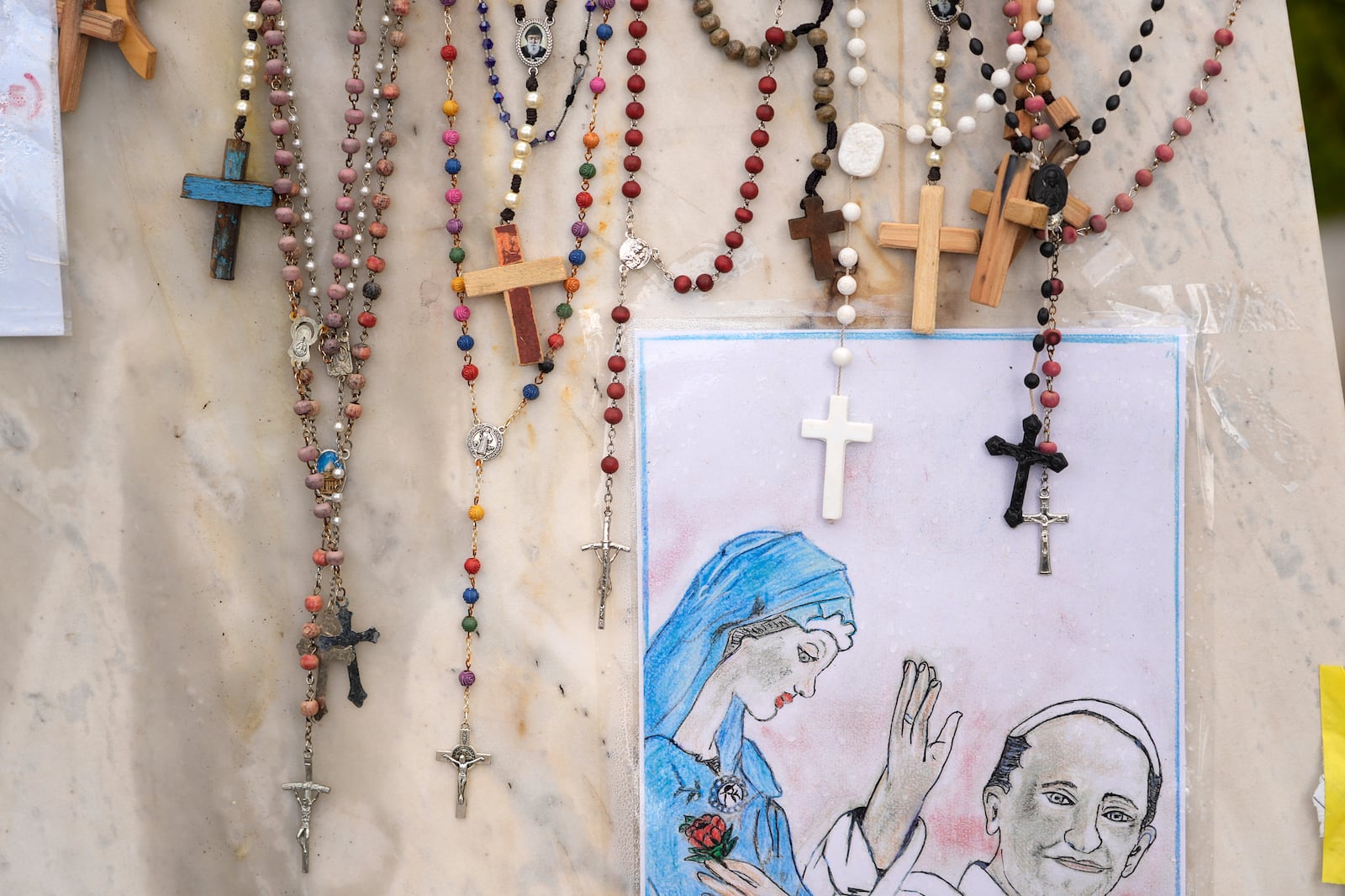 Rosaries are seen next to a drawing of Pope Francis outside the Agostino Gemelli polyclinic in Rome, Sunday, March 16, 2025. (AP Photo/Gregorio Borgia)