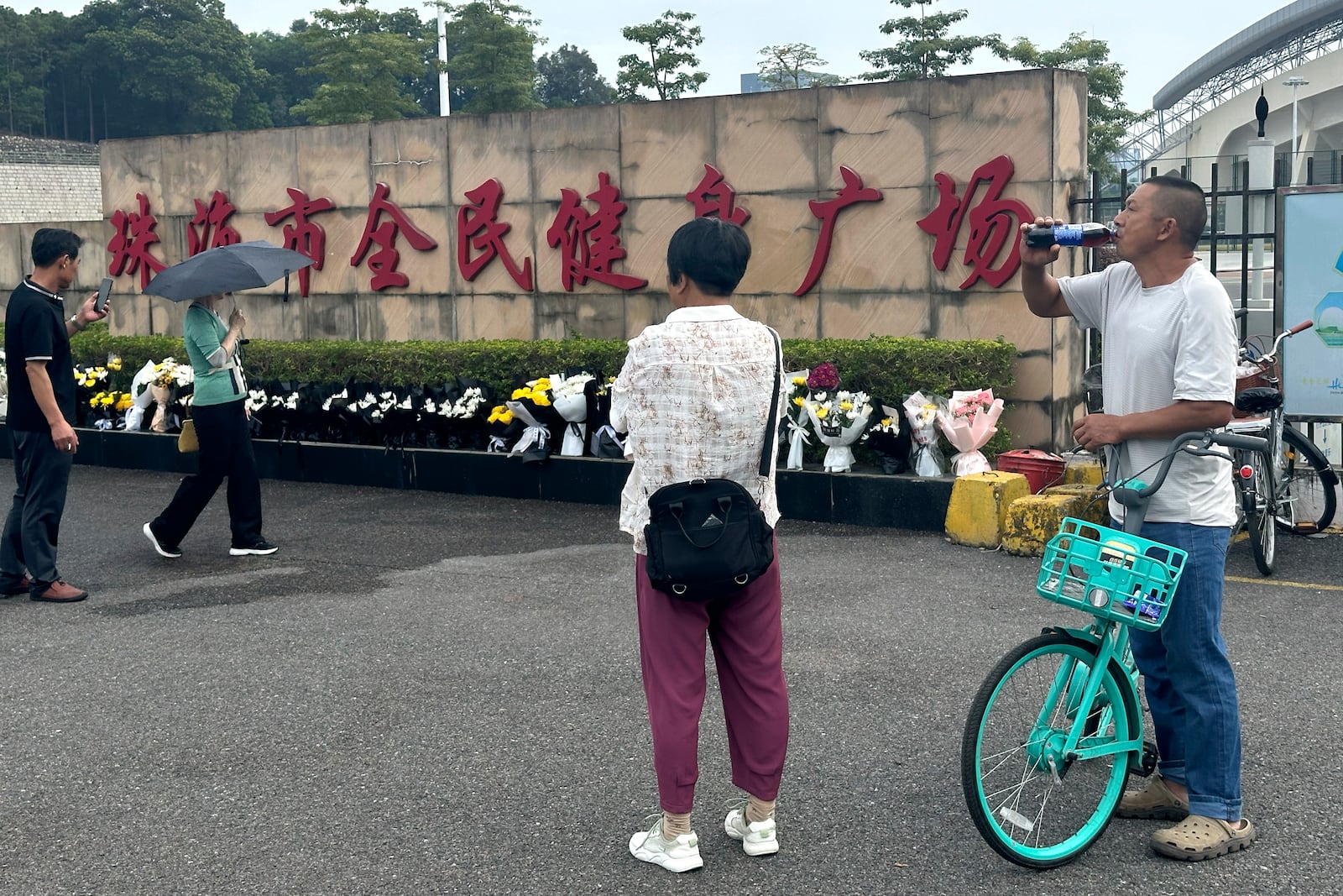 Residents look at flowers laid outside the "Zhuhai People's Fitness Plaza" where a man rammed his car into people exercising at the sports center, in Zhuhai in southern China's Guangdong province on Wednesday, Nov. 13, 2024. (AP Photo/Ng Han Guan)