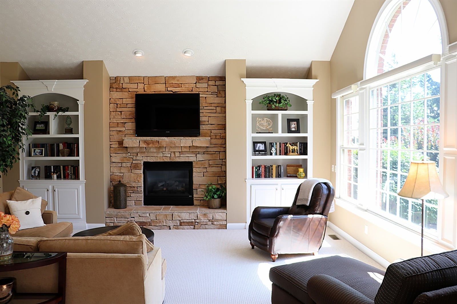 A cathedral ceiling peaks above the great room. A stack-stone gas fireplace has a raised stone hearth and stone mantle. The fireplace is flanked by built-in bookcases and cabinetry, which have arched top-shelf accents that match the Palladian window. CONTRIBUTED PHOTO BY KATHY TYLER